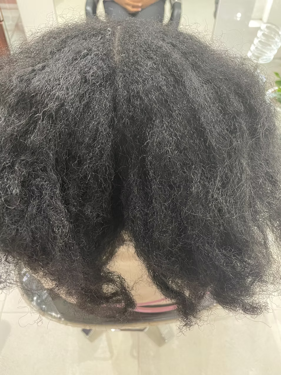 Close-up of a person with thick, curly, black hair, sitting in a salon chair.