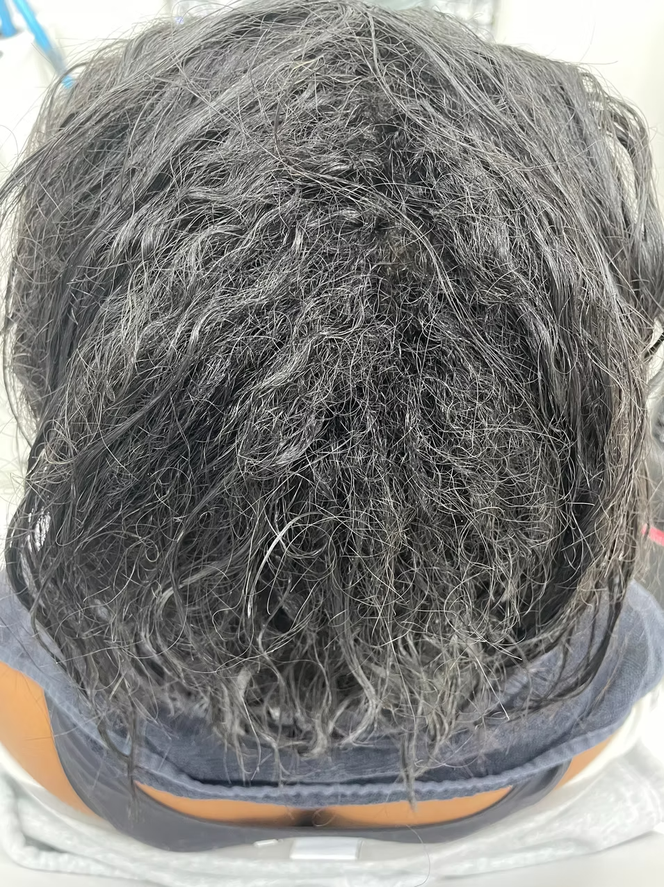 Close-up of a person's head with wet, curly gray hair viewed from above.