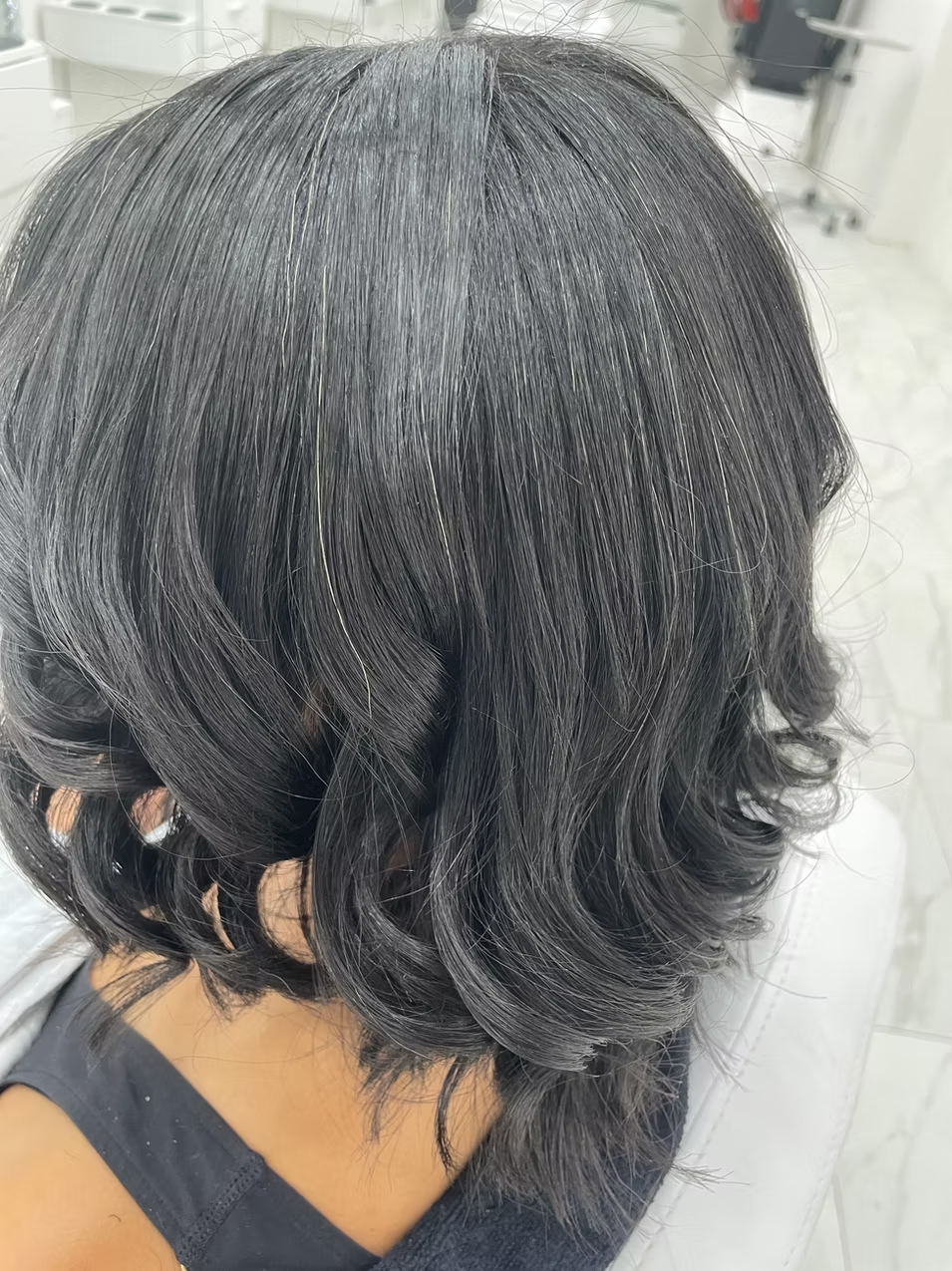 Close-up of a person's black hair with loose curls, taken indoors in a bright setting.