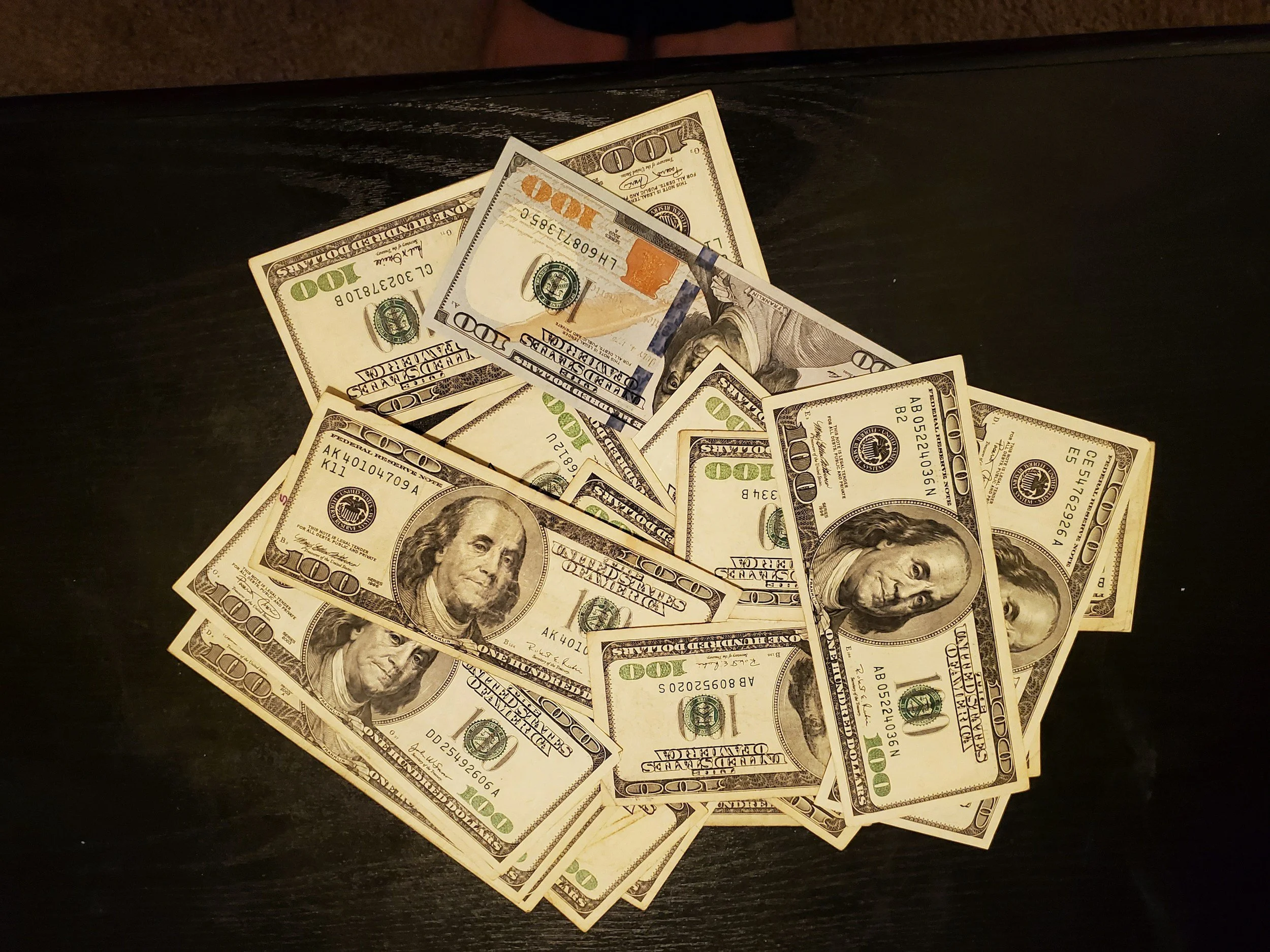 Pile of assorted U.S. one hundred dollar bills scattered on a dark wooden surface.