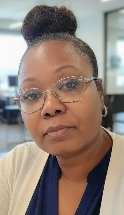 A woman with glasses and earrings, with hair styled in a bun on top of her head, sitting in an office environment.