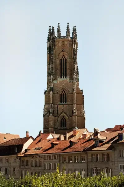 A tall Gothic-style church tower with ornate spires in Fribourg, rising above buildings with red-tiled roofs.