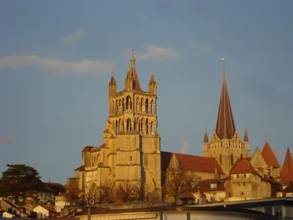 View of historic church in Lausanne with tall spire and ornate towers in a European city under a blue sky.