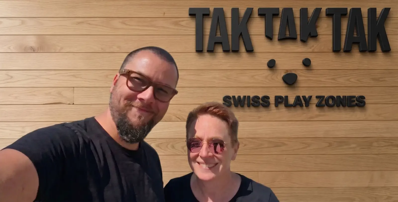 Homme et femme qui sourient avec panneau tak tak tak au fond