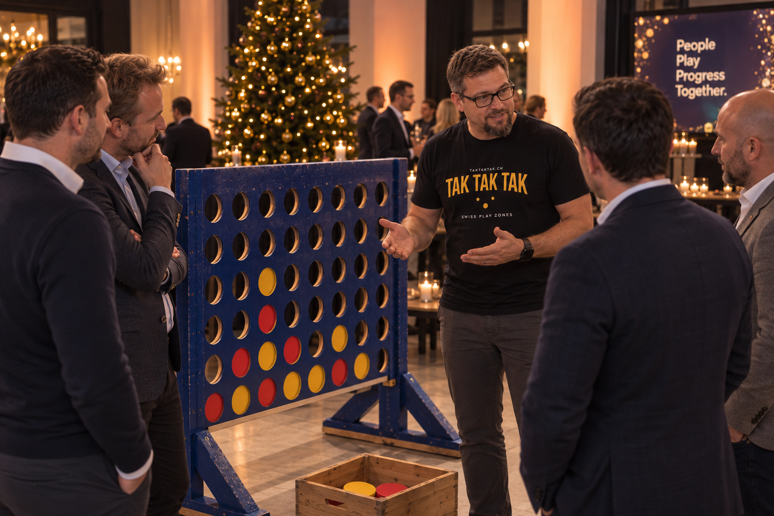 A man demonstrating a giant Connect Four-style game to a group of four men at a holiday party. The game has red and yellow circular discs, with some discs already placed in the grid. Christmas trees and lit candles are visible in the background.