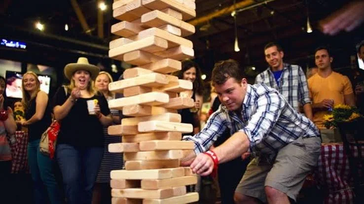 Participant jouant au Jenga géant pendant que d’autres invités regardent et réagissent
