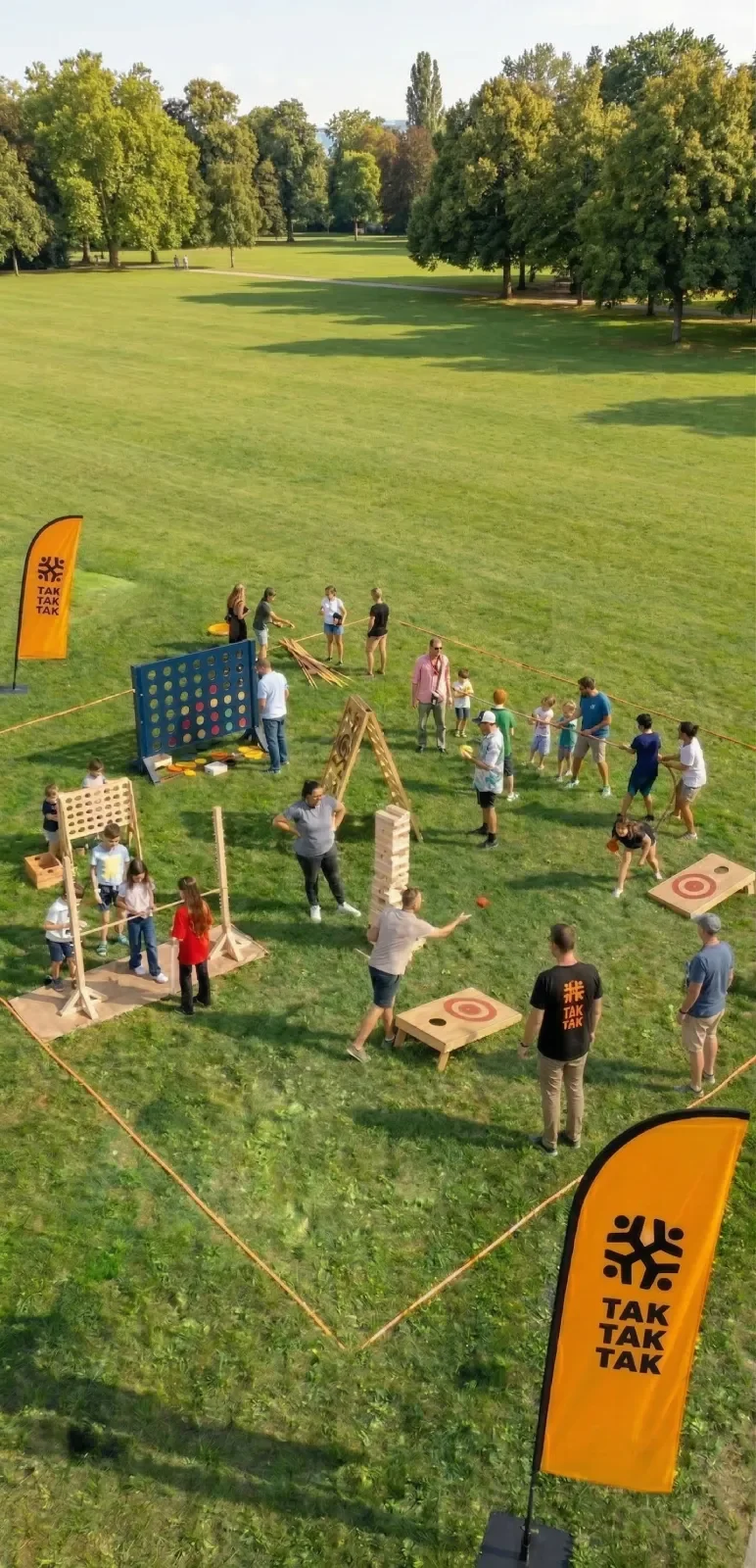 Des gens jouent des jeux en bois géants, comme puissance quatre, cornhole, jenga géant, tir à la corde, mikado géant dans une zone cée par l'entreprise événementielle Tak Tak Tak