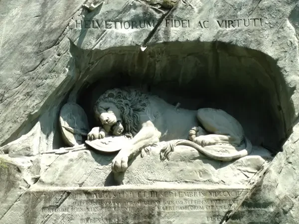A carved stone relief of a lion lying down inside a cave-like structure with Latin inscriptions above and below in Lucerne.