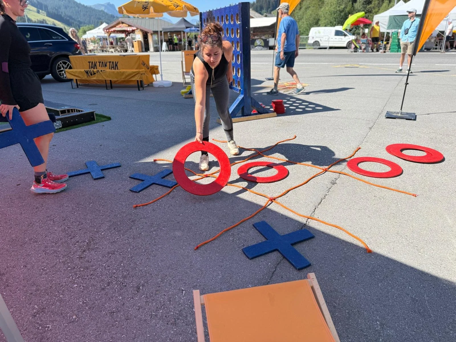 People playing giant outdoor Tic-Tac-Toe game at a festival or event on a sunny day in a mountain town parking lot.