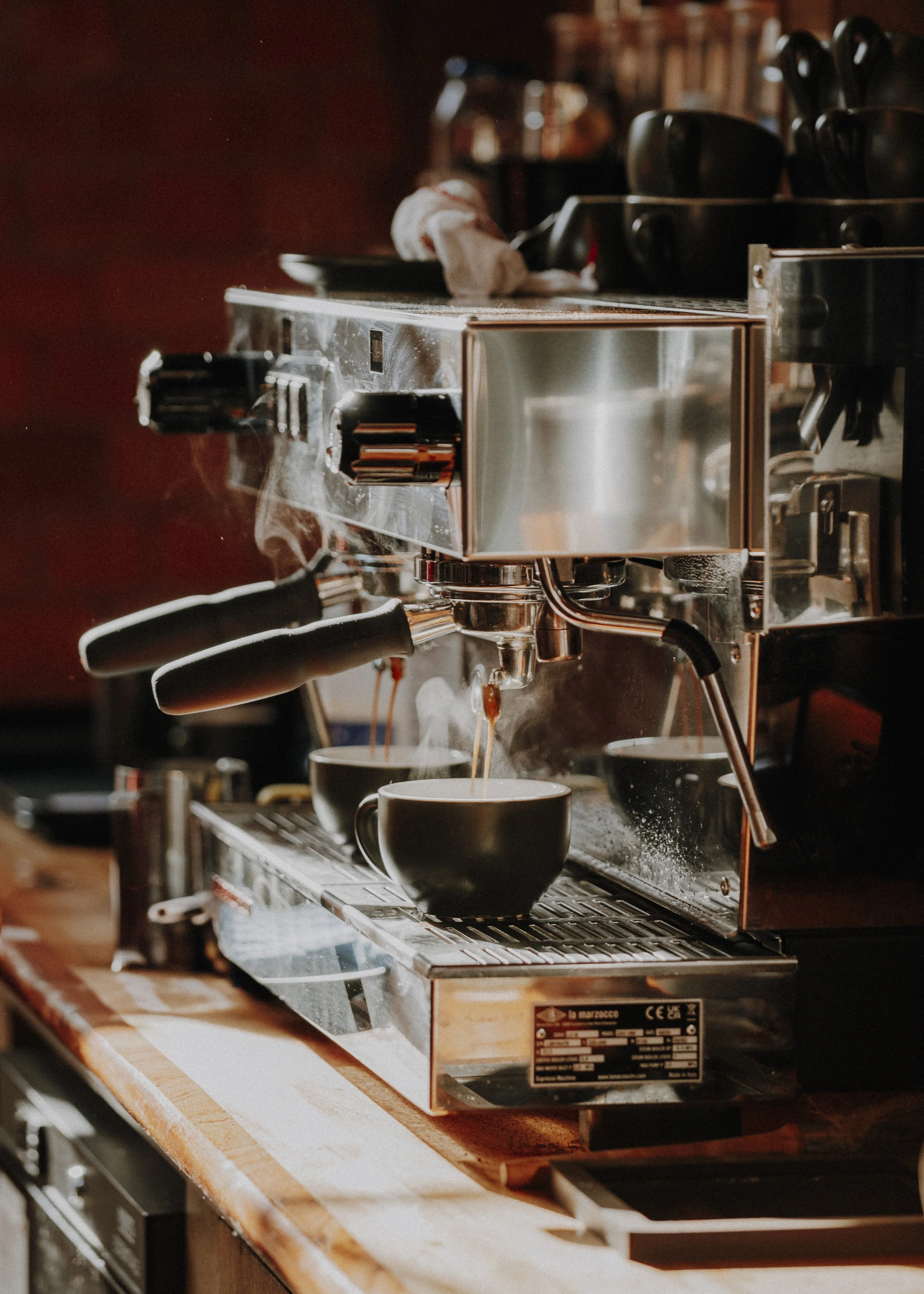 A close-up view of a professional espresso machine brewing coffee into two black cups on a wooden countertop.
