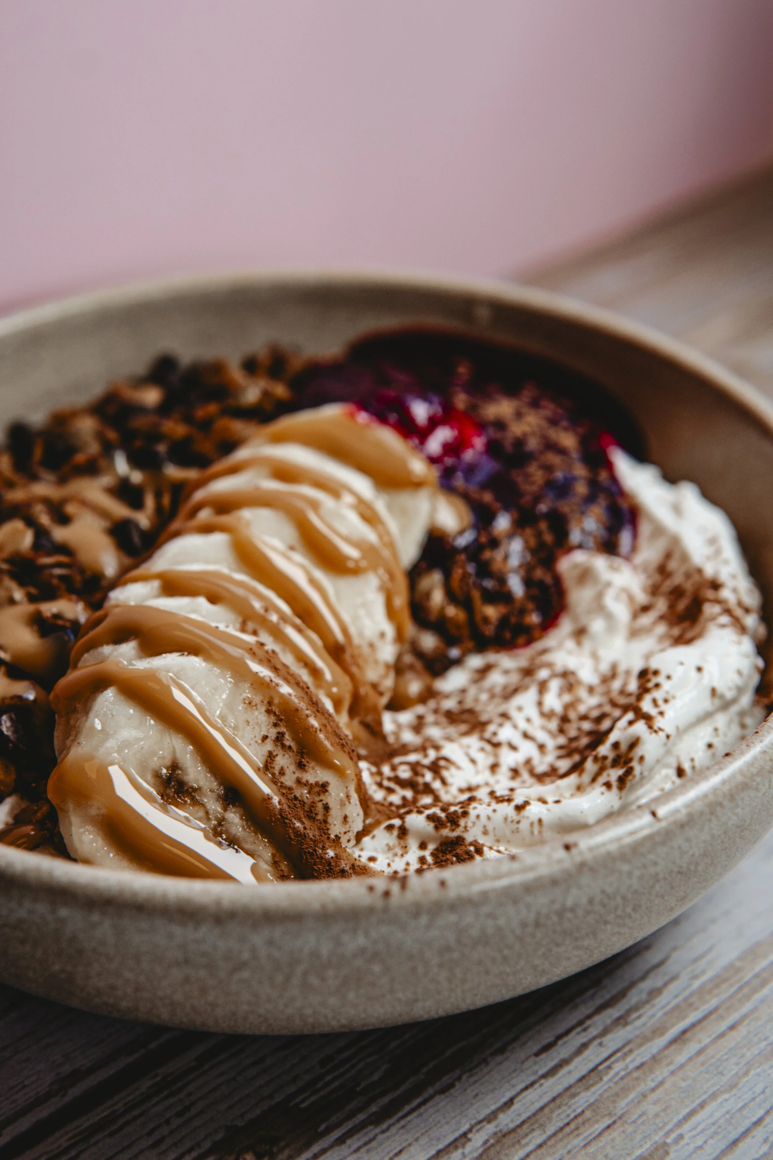 Close-up of a bowl of assorted ice cream topped with caramel sauce, chocolate shavings, and fruit compote.