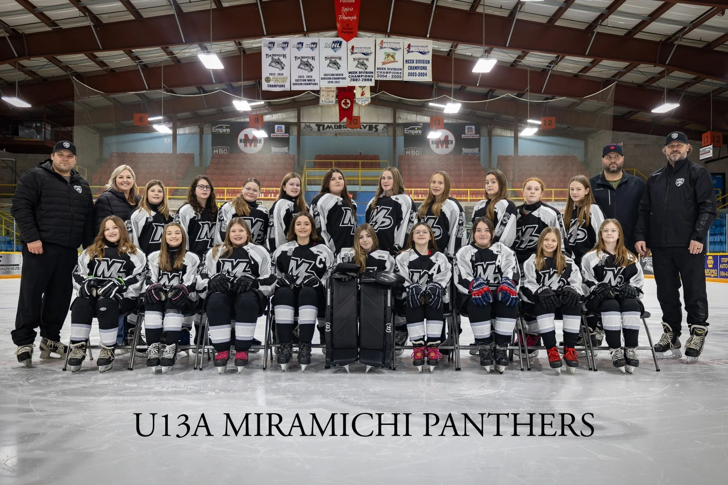 A youth hockey team called U13A Miramichi Panthers posing for a team photo on an ice rink, with coaches and players in black and white jerseys, hockey gear, and helmets, in an indoor hockey arena.