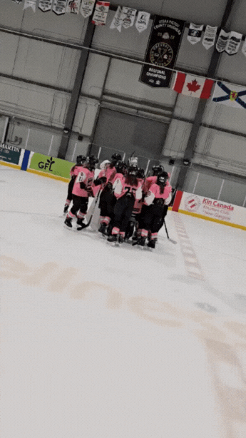A group of ice hockey players in pink jerseys huddled together on the ice rink.