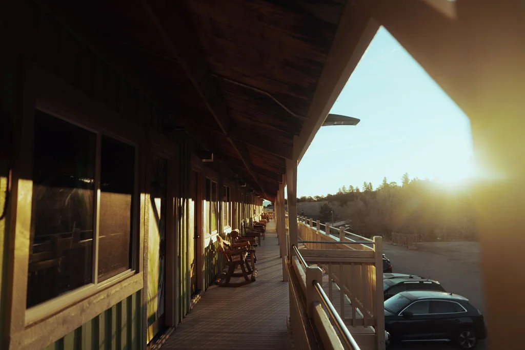 Sunset over a wooden balcony with cars parked beneath, overlooking a hillside with trees.