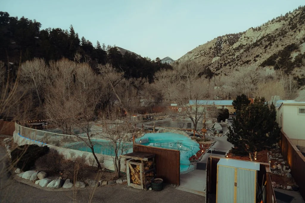 Mountain landscape with a backyard featuring a swimming pool, hot tub, trees, and surrounding houses in a hilly area.