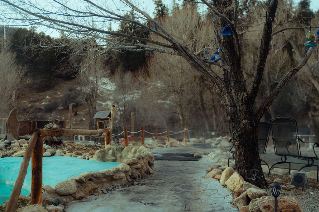 Empty outdoor hot spring surrounded by rocks, bare trees, and benches in a natural setting.