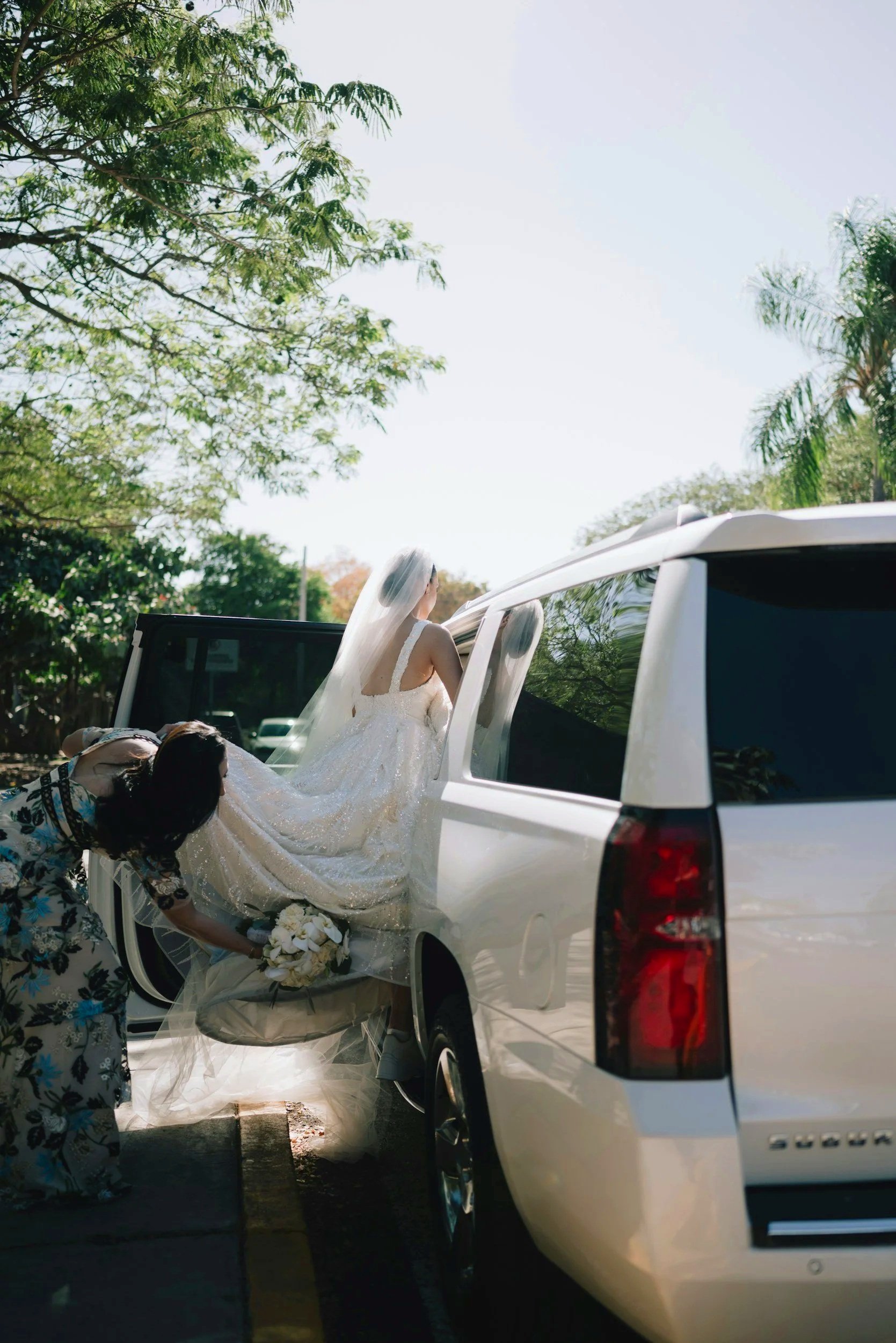Bride in a wedding gown entering a white Cadillac Escalade