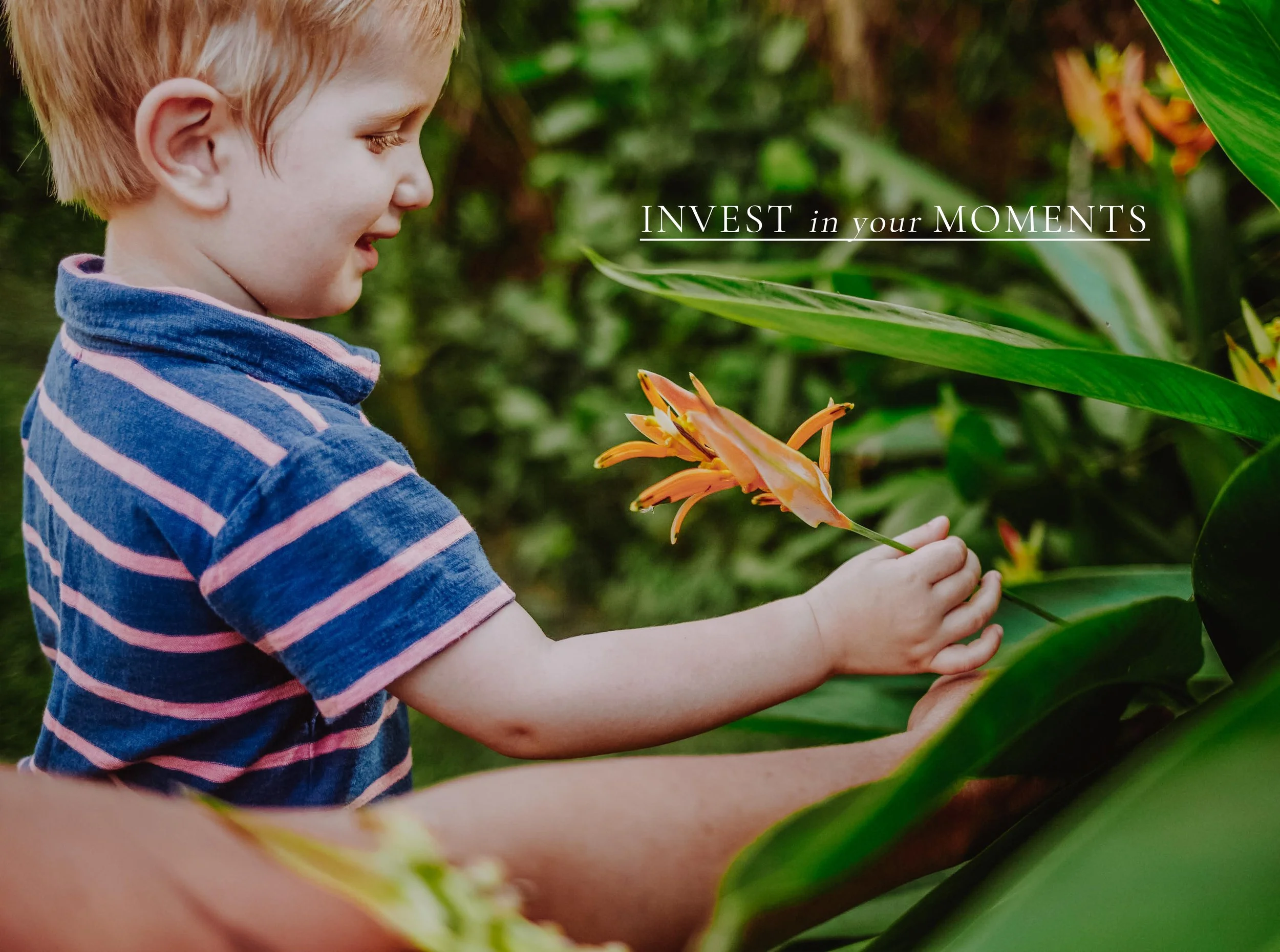 A young child in a striped blue and pink shirt holding orange lilies in a lush green garden.