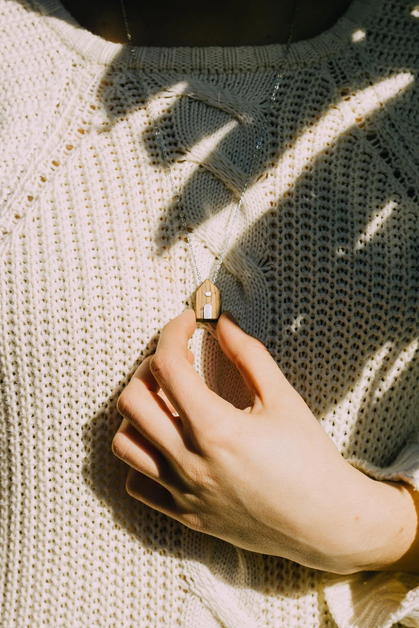 Close-up of a person wearing a knit sweater and holding a necklace with a small house pendant.