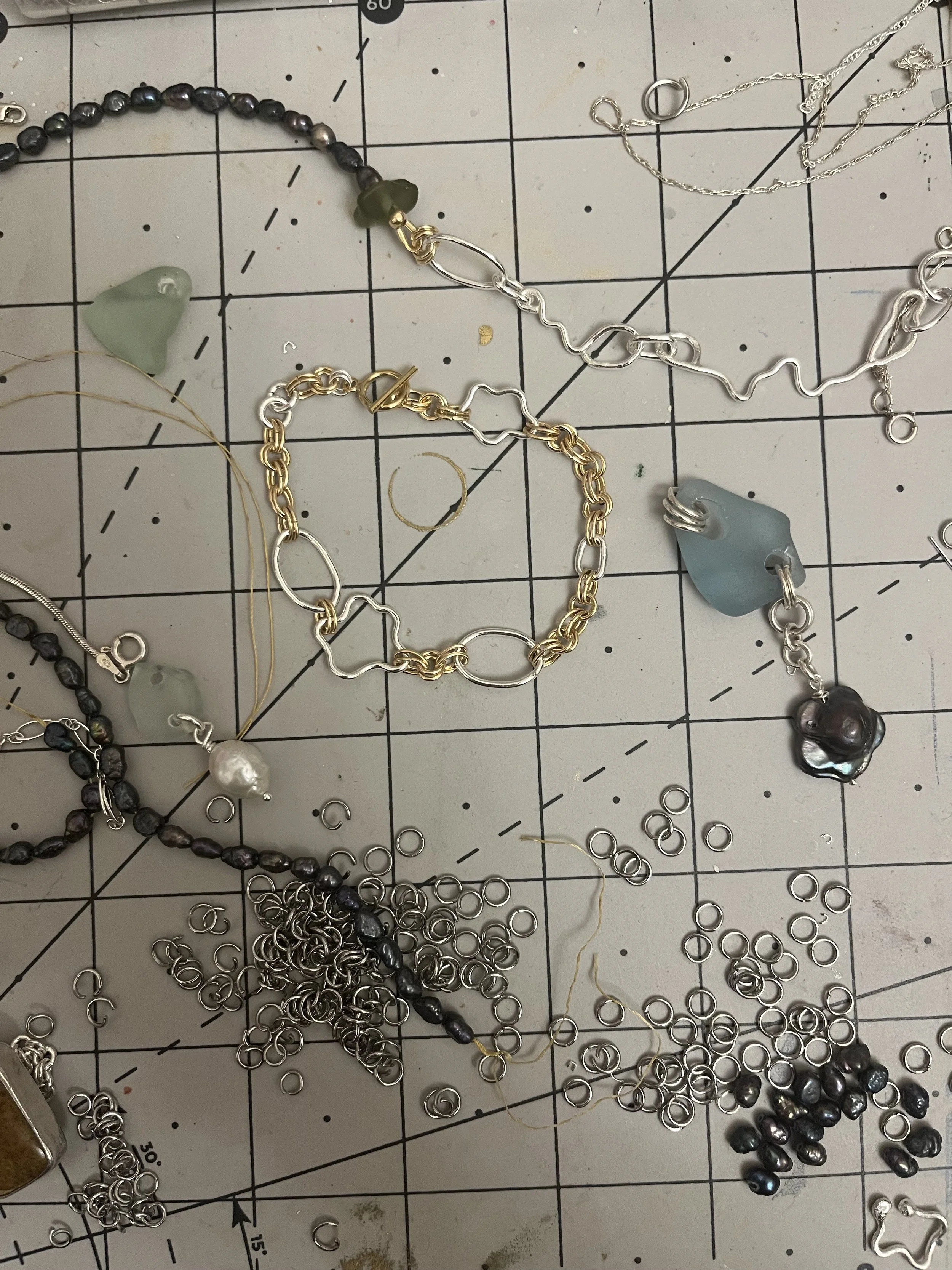 Assorted jewelry pieces, including links, beads, and pendants, scattered on a gridded work surface.