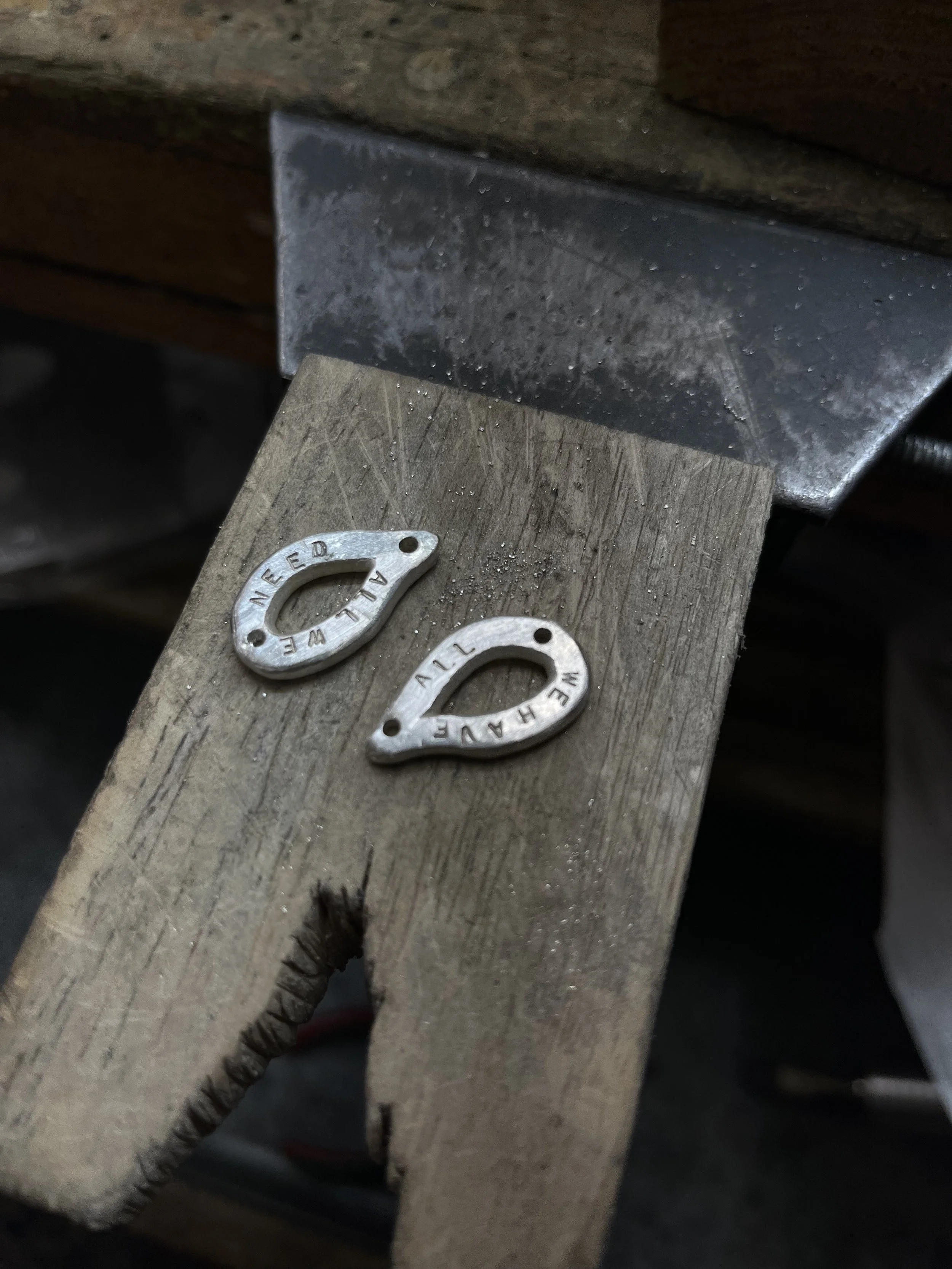 A metal object with the word "ALLEN" engraved on it, placed on a wooden surface next to a piece of metal with a rough surface, in a workshop or craft setting.