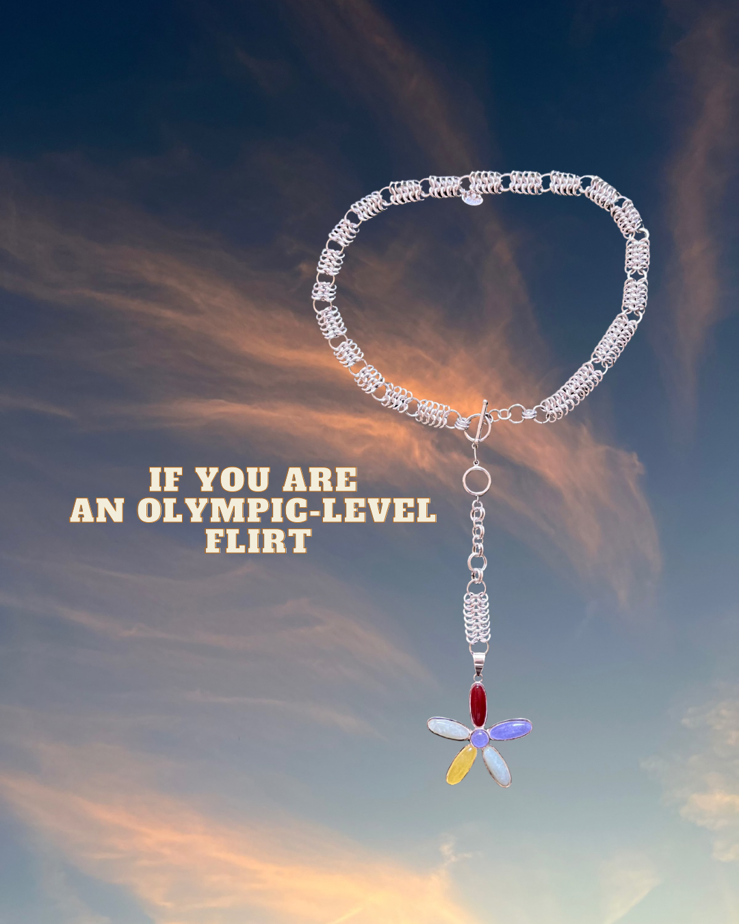 A silver necklace with a flower-shaped pendant featuring colorful stones is suspended in the sky during sunset, with the text 'If you are an Olympic-level flirt' overlaid on the image.