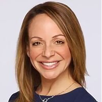 A woman with shoulder-length reddish-brown hair smiling, wearing a dark top and a necklace, against a light background.