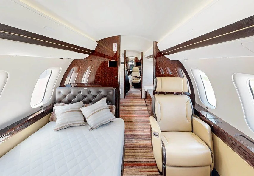Luxury private airplane interior with a bed and seating area, wood paneling, and windows.