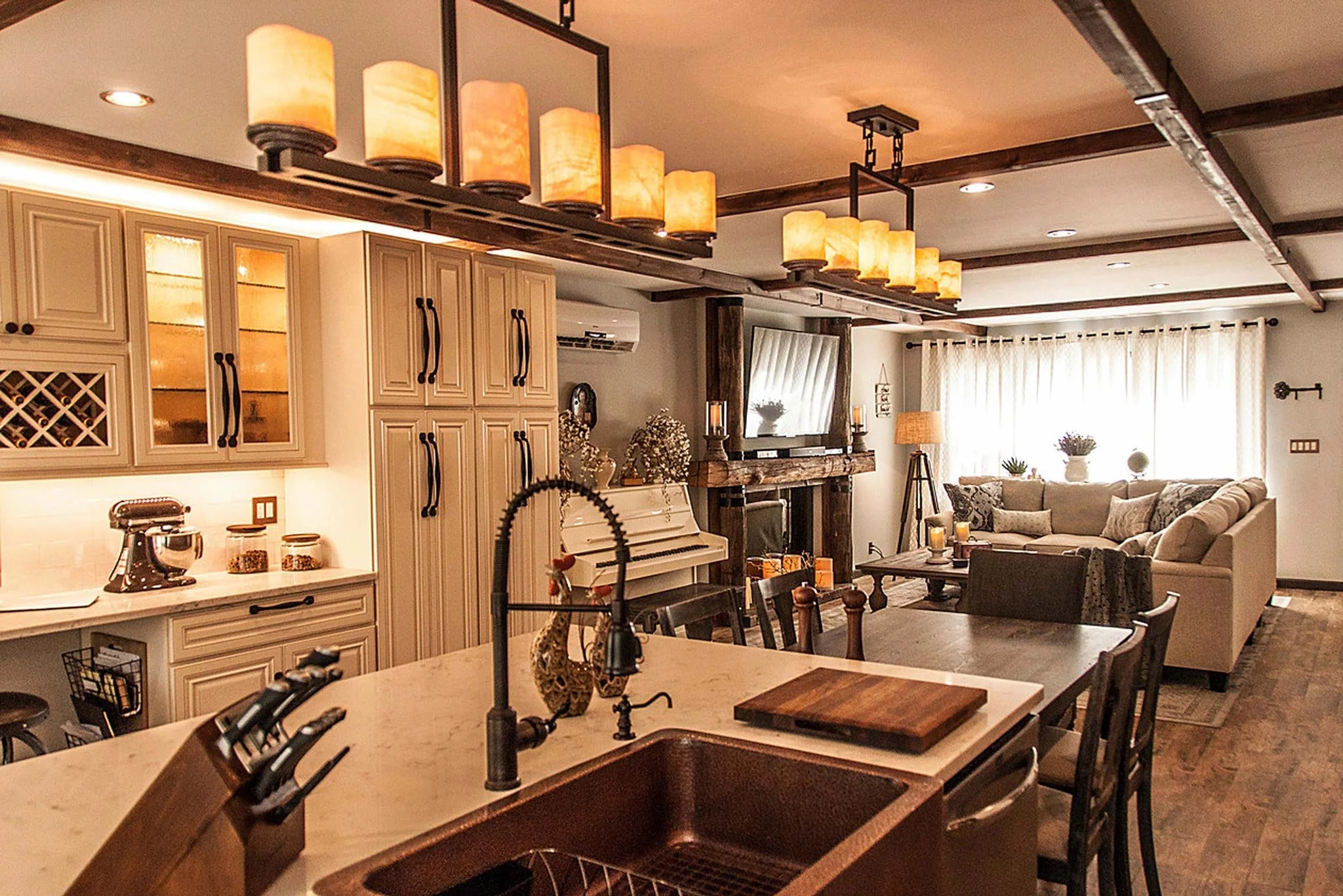 Open-concept living room and kitchen with warm lighting, beige cabinets, wooden accents, and a cozy seating area.