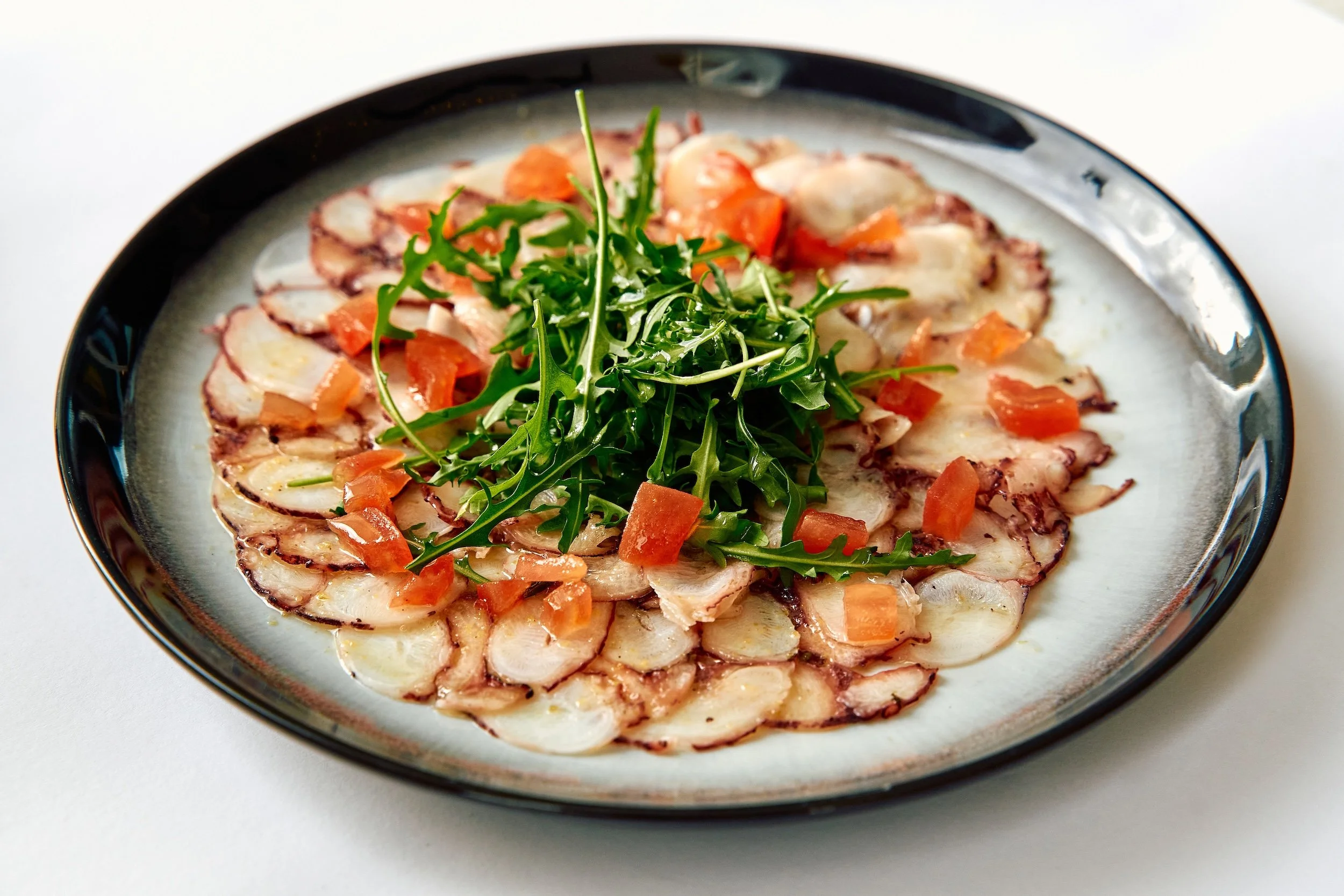 Plate of carpaccio with thinly sliced raw meat garnished with arugula and diced tomatoes.