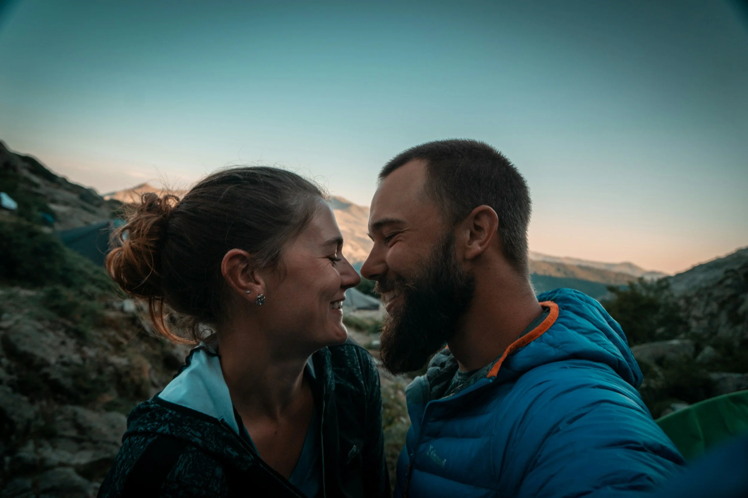 A smiling couple touching foreheads outdoors during sunset.