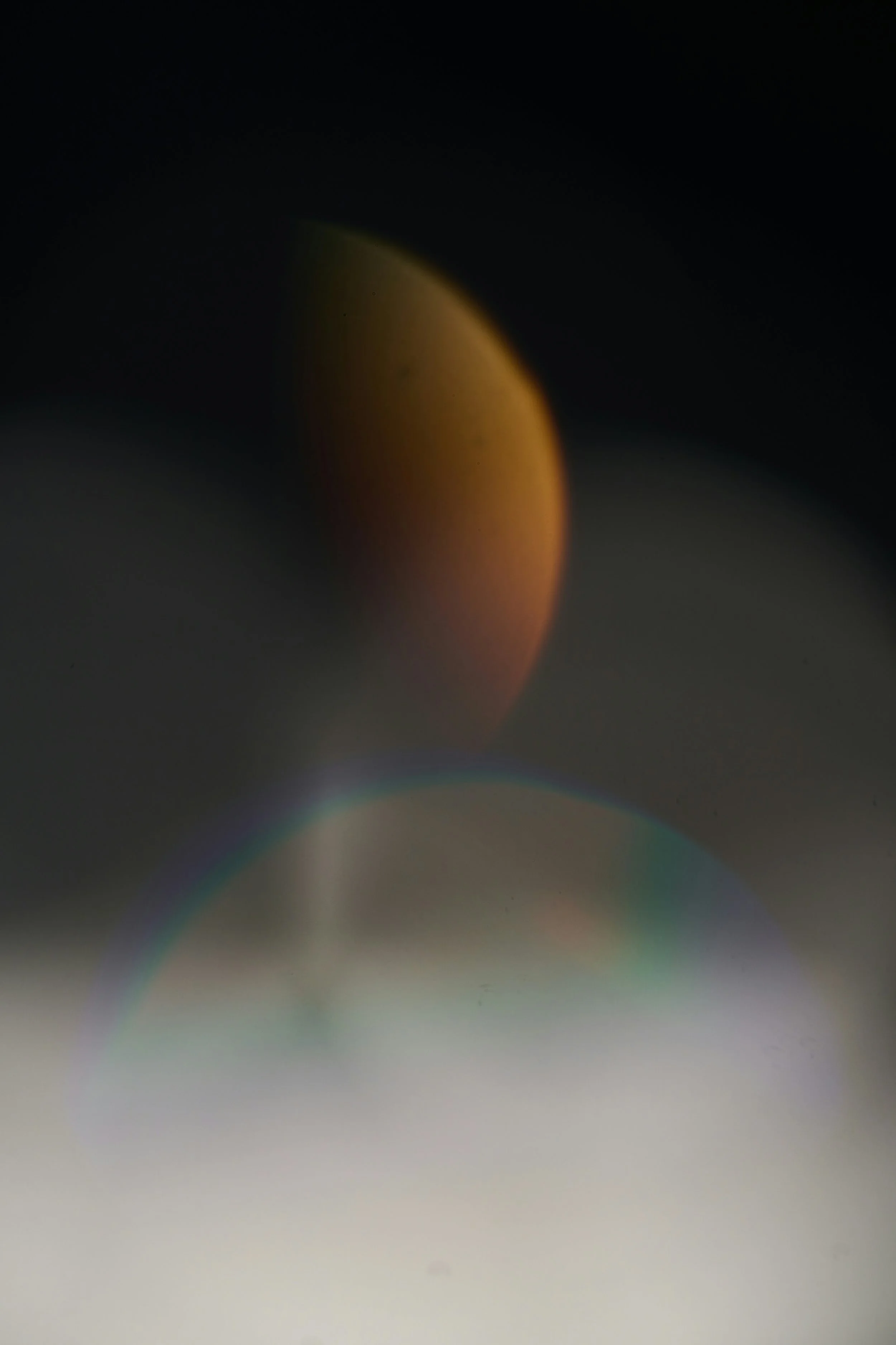 Close-up abstract photograph of a moon, with colorful light artifacts and a blurred surface, dark background.