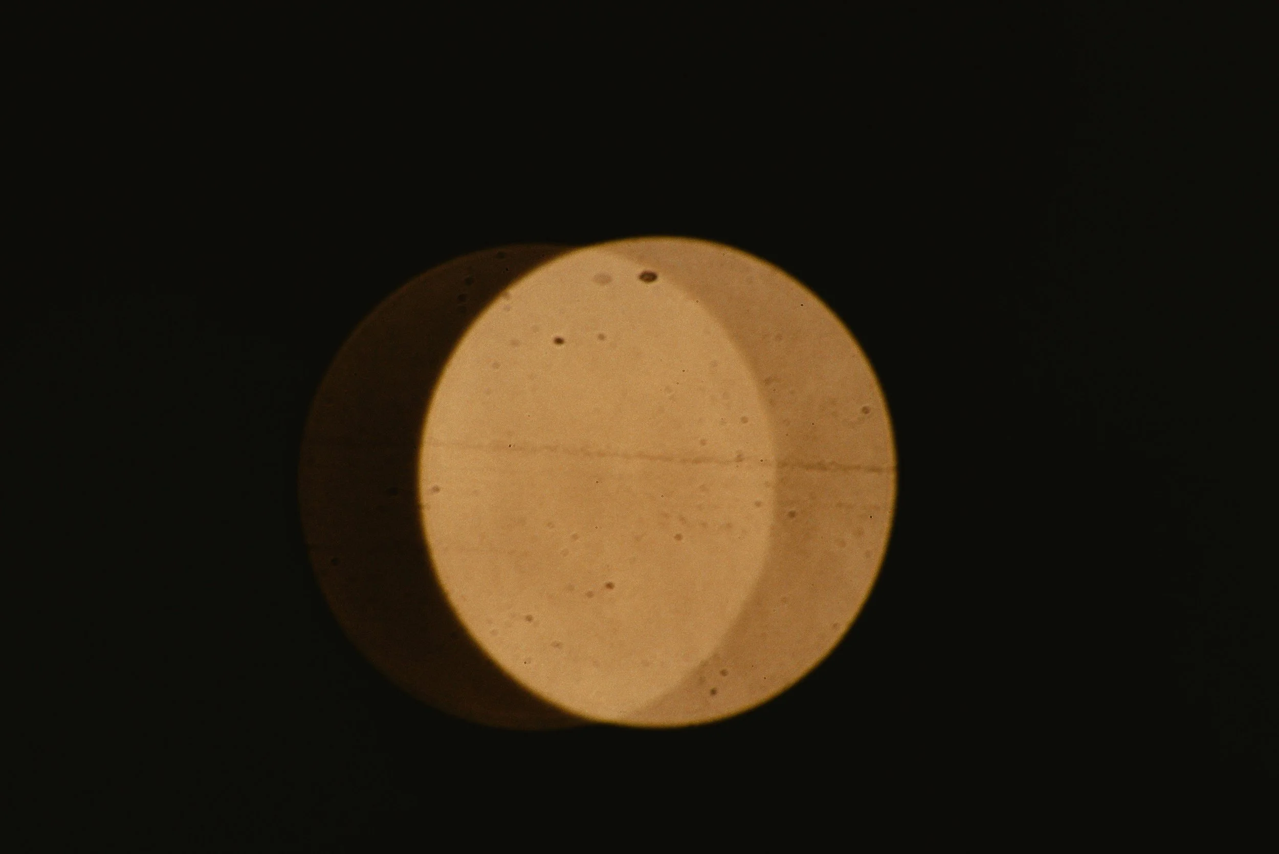 Close-up of a round light source in darkness, with visible specks and a shadowed side.