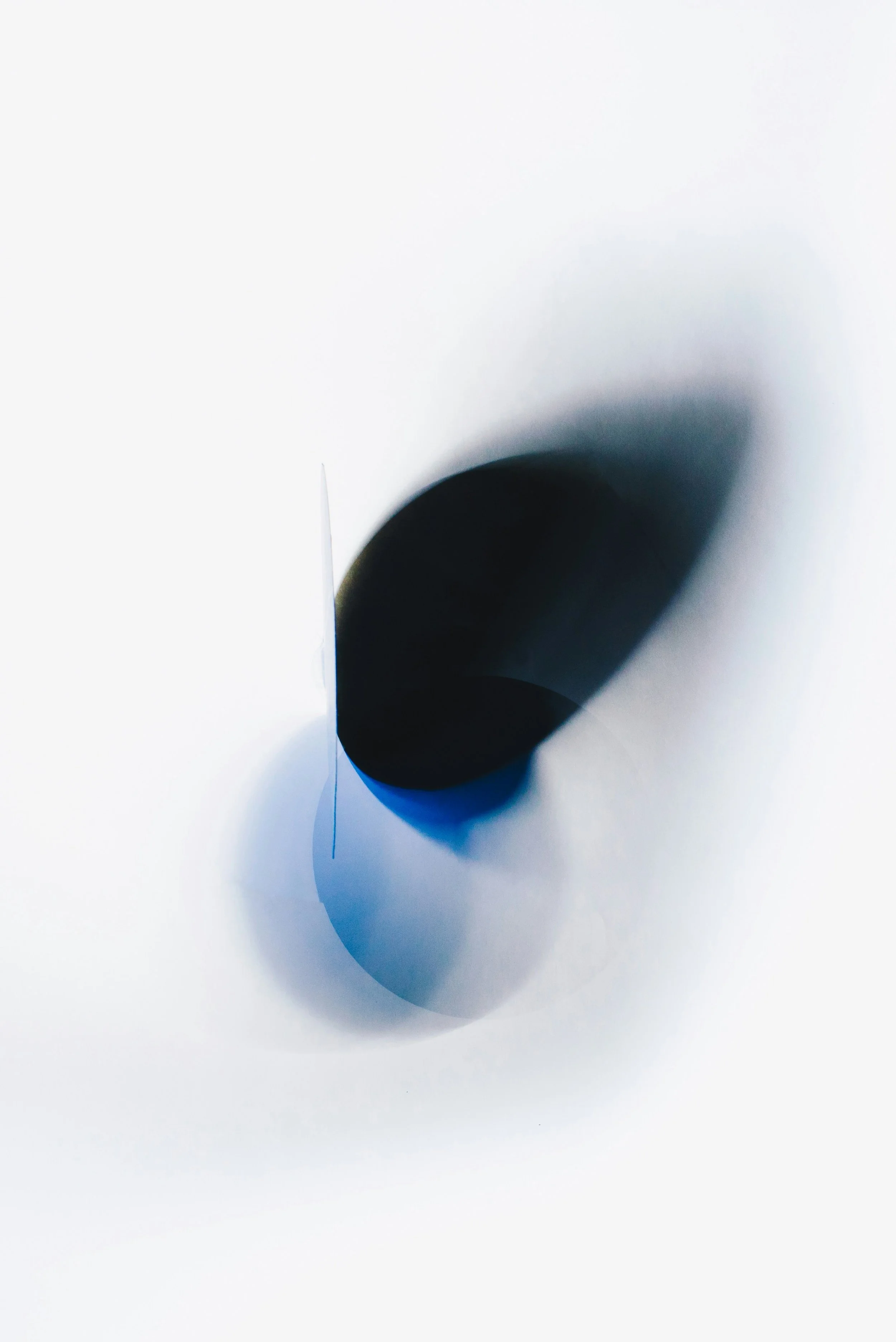 A minimalist abstract image featuring a black circular object with shadows and a blue hue, set against a white background.