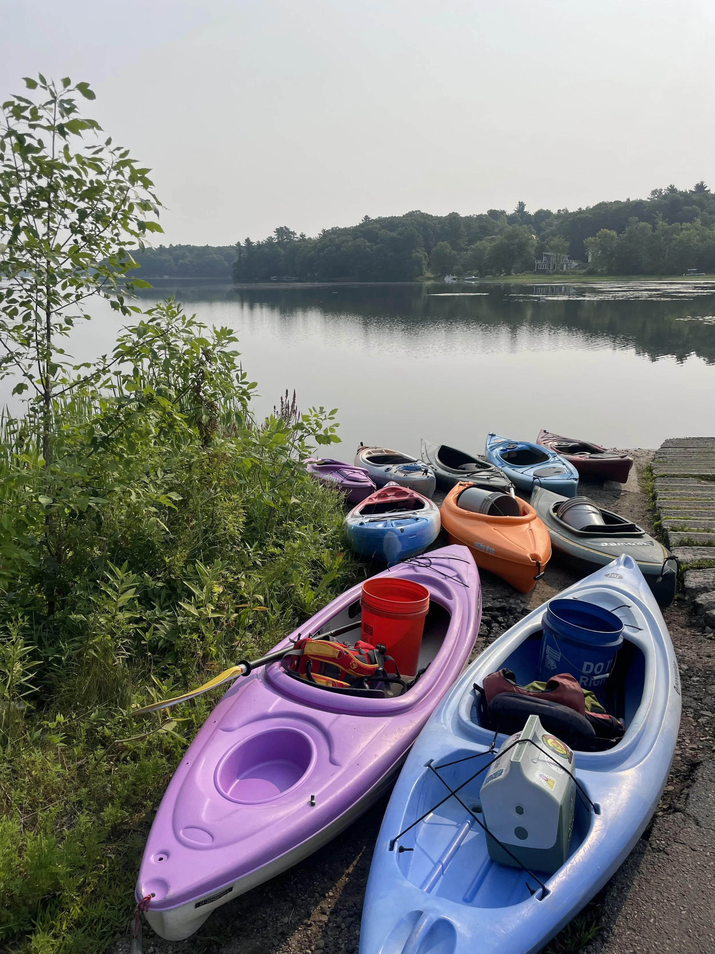 10 kayaks loaded with survey gear at a boat launch with a lake in the background