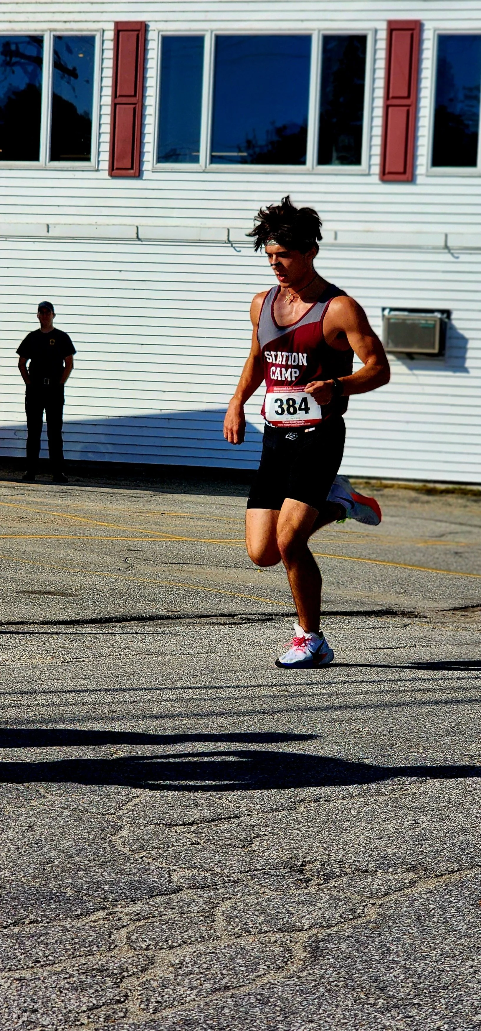 A man, wearing a maroon and grey tank top with black shorts, running