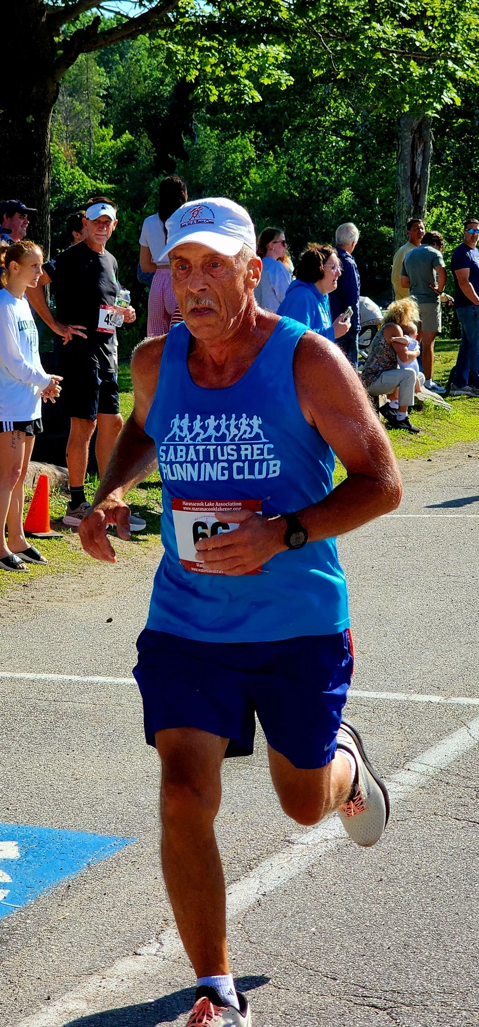 A man wearing a blue tank top with blue shorts running with a crowd standing in the background