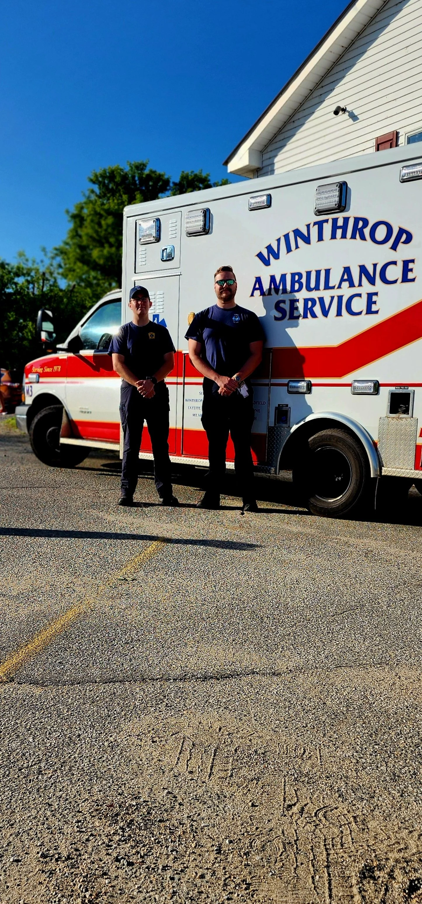 Two men in EMT uniforms standing in front of an ambulance