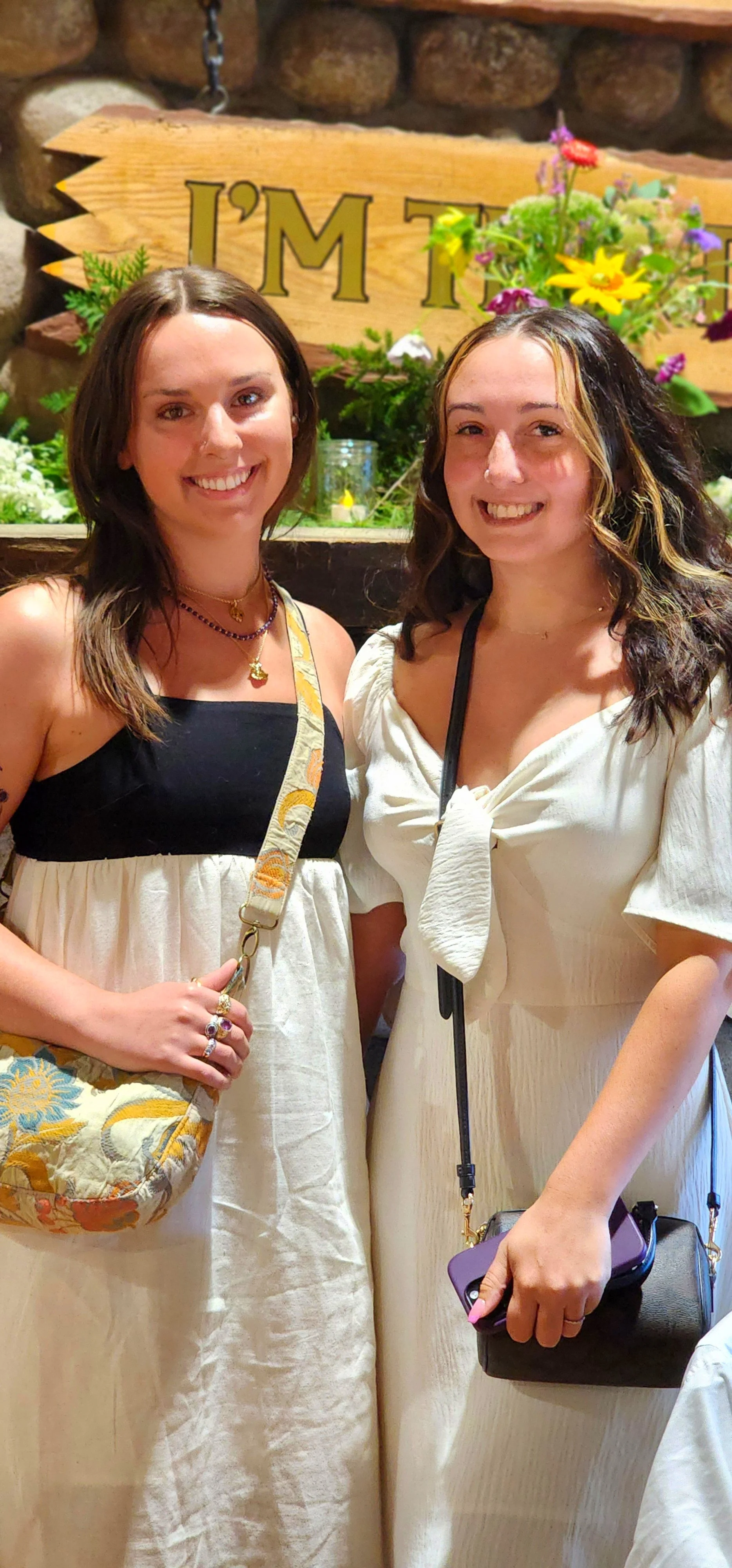 Two women, the one on the left wearing a black and white dress and the one on the right wearing a white dress, smiling at the camera