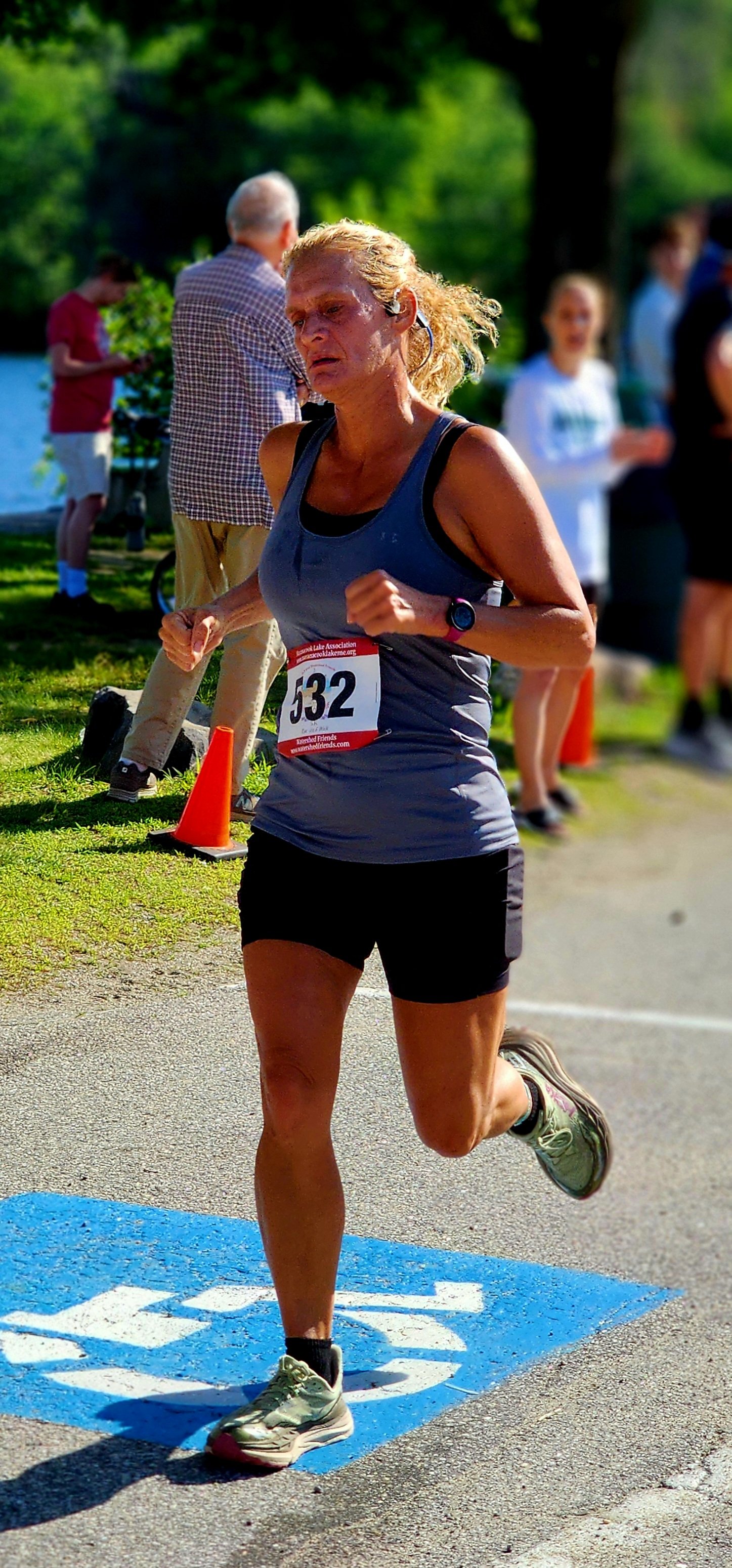 A woman wearing a grey tank top and black shorts running with a crowd standing in the background