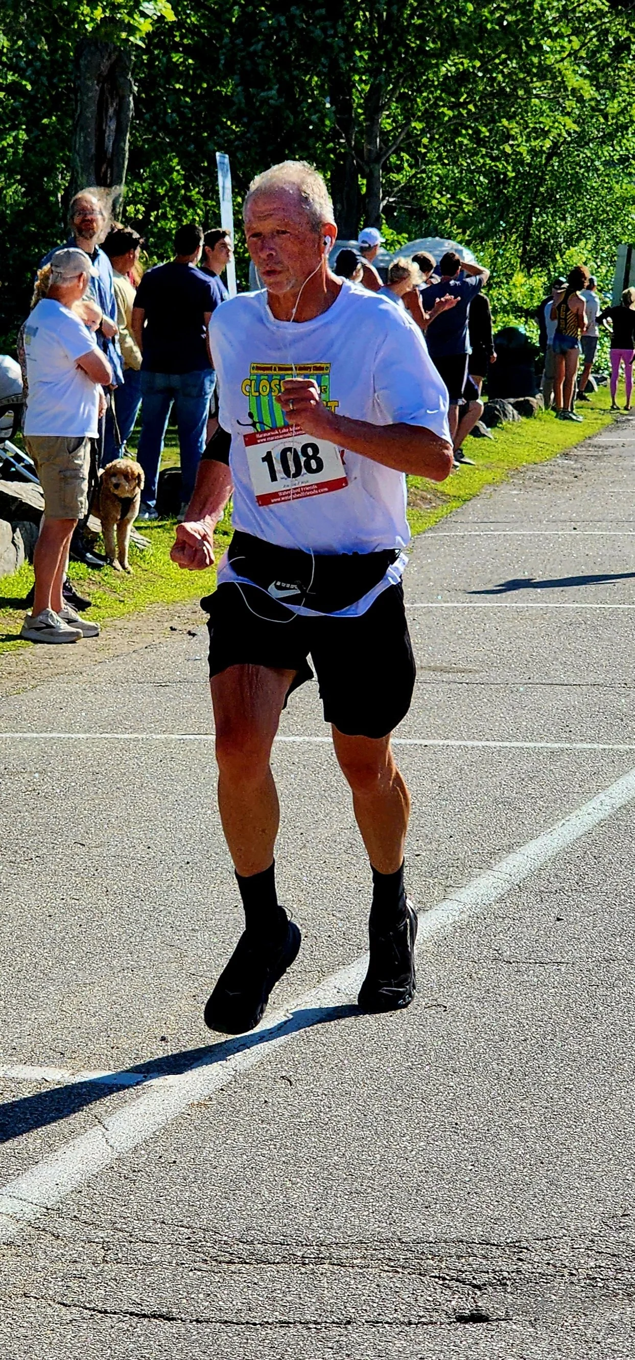 A man wearing a white t-shirt and black shorts running with a crowd standing in the background