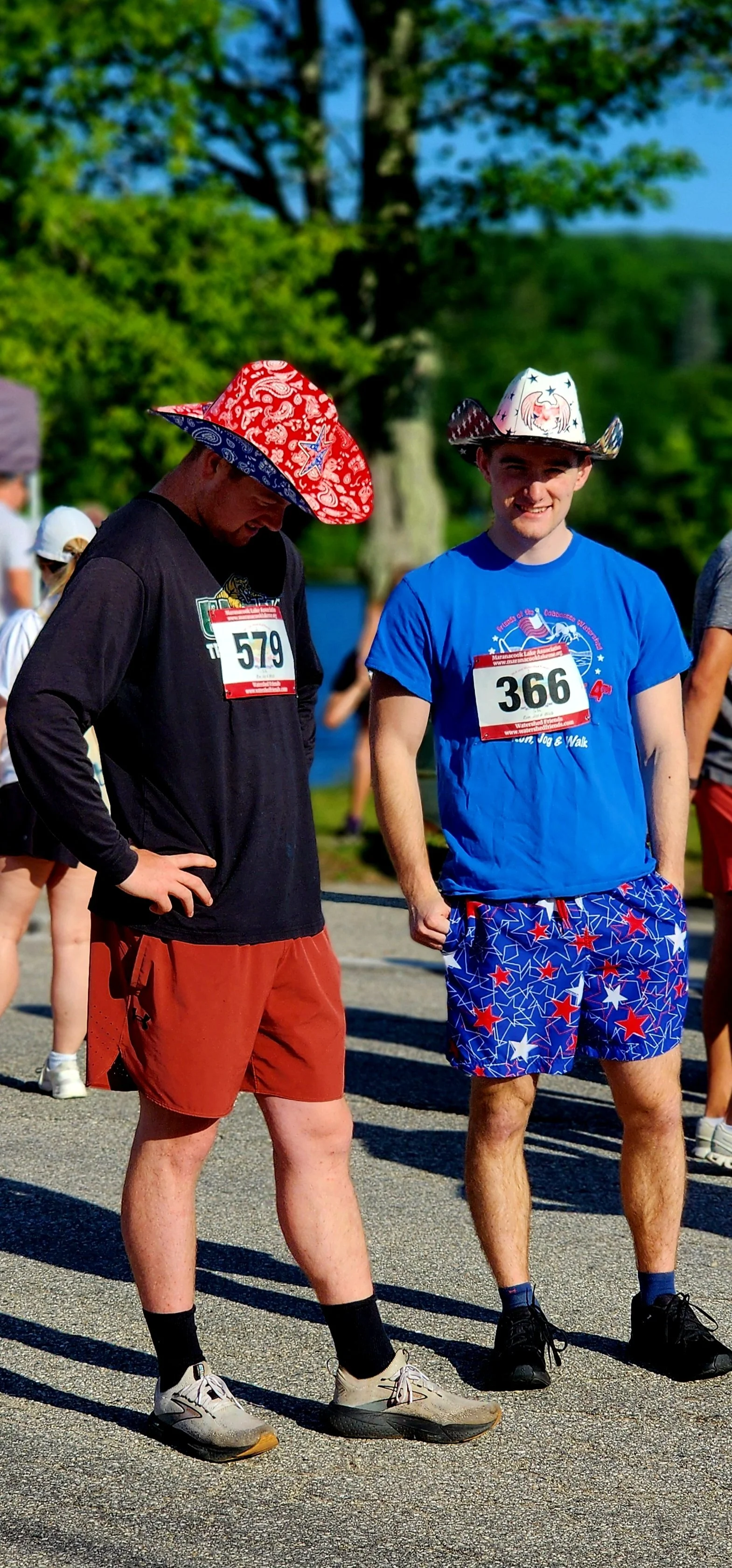 Two men in patriotic cowboy hats, one wearing a black long sleeve shirt and red shorts, the other wearing a blue t-shirt and blue shorts