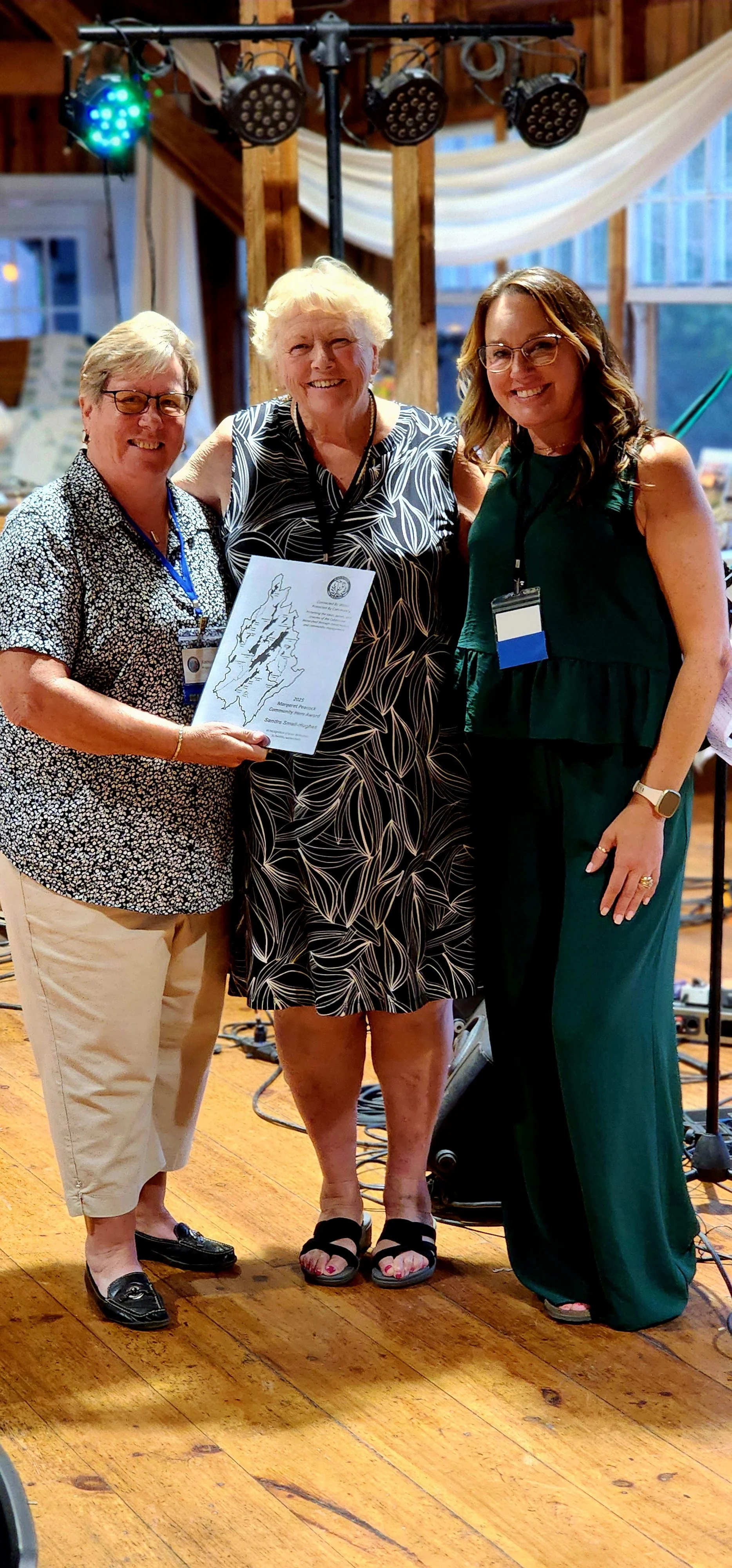 Three women smiling at the camera, the one on the left holding a plaque