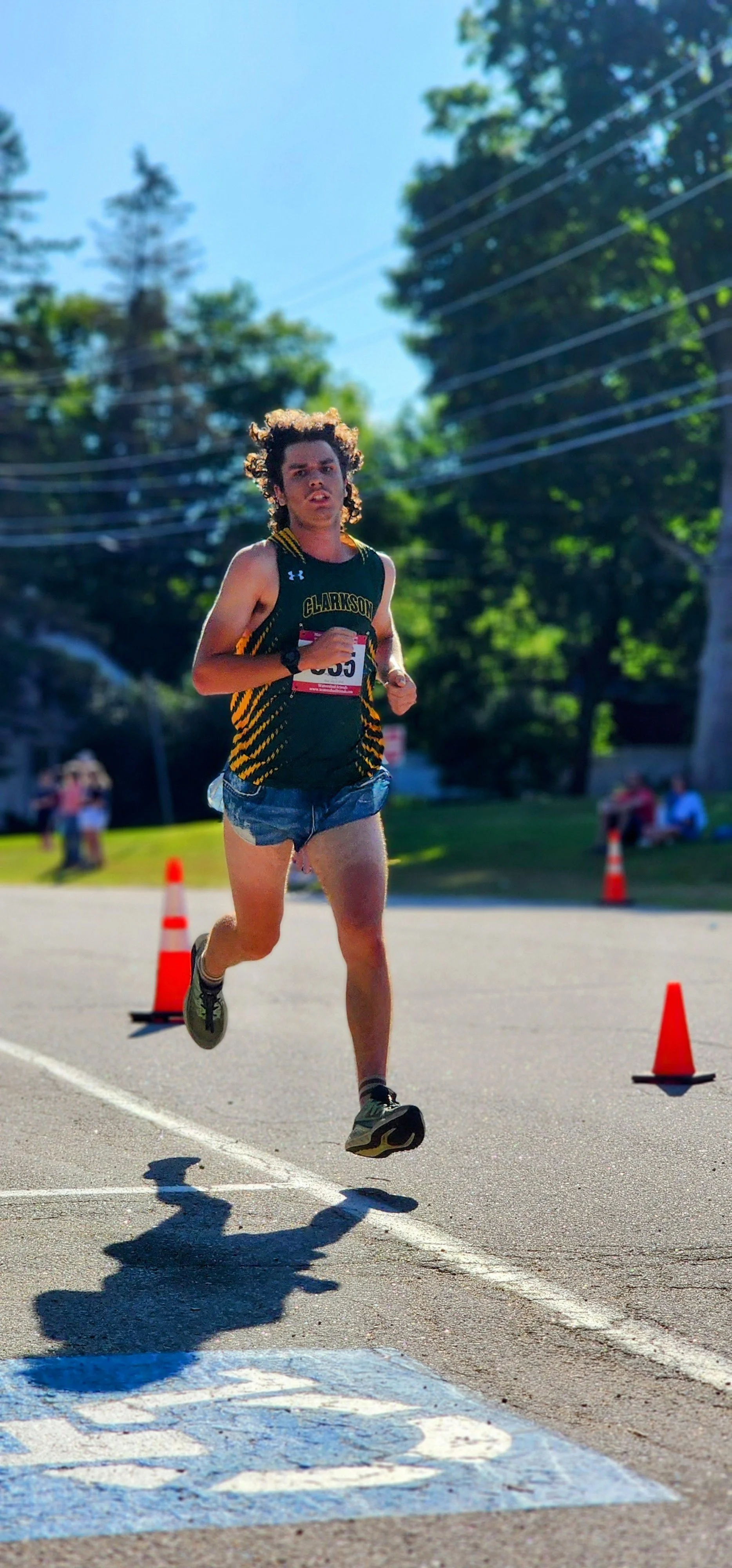 A man wearing a green and yellow tank top and blue shorts running