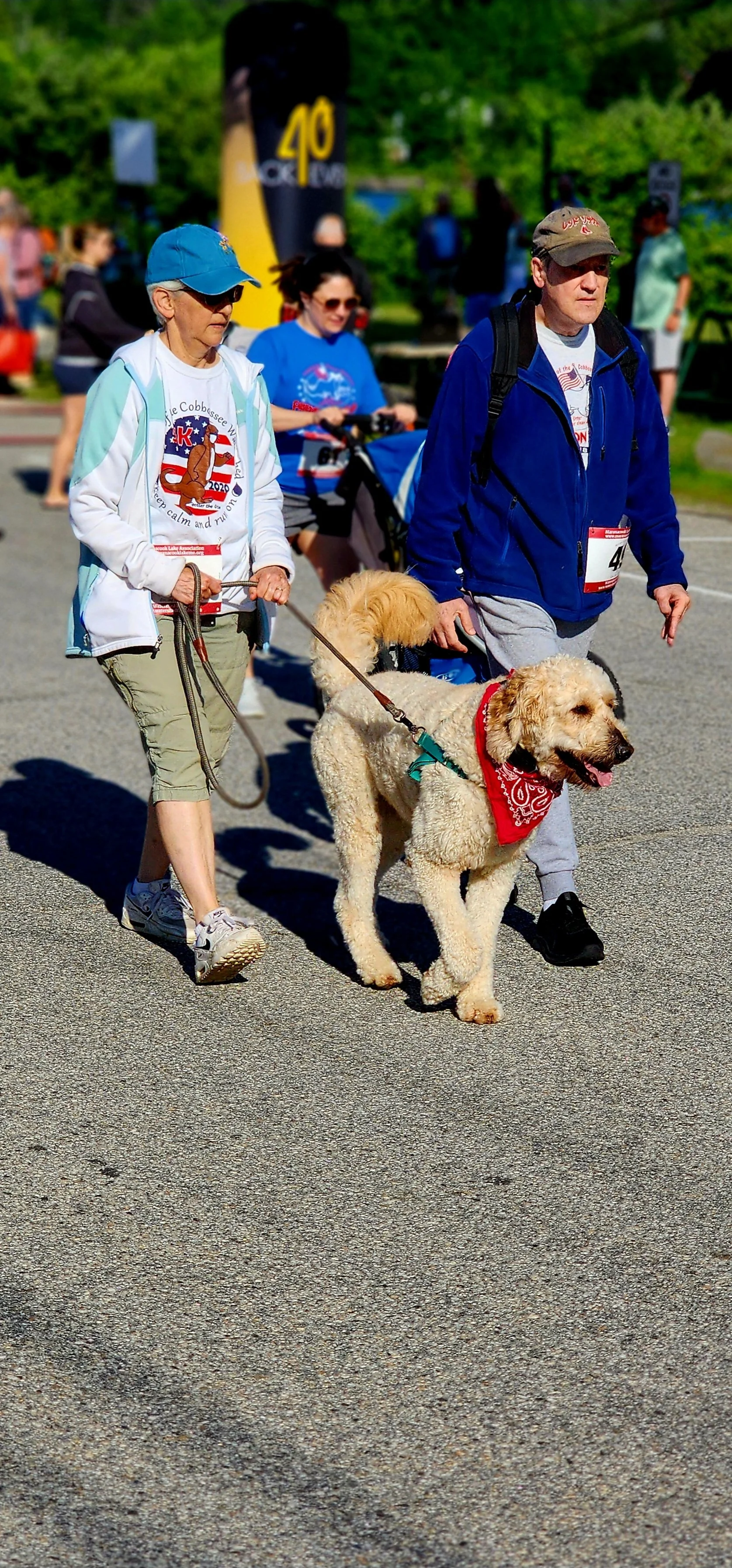 A woman wearing a teal and white sweatshirt with khaki pants walking a dog with a man wearing a blue sweatshirt and grey pants