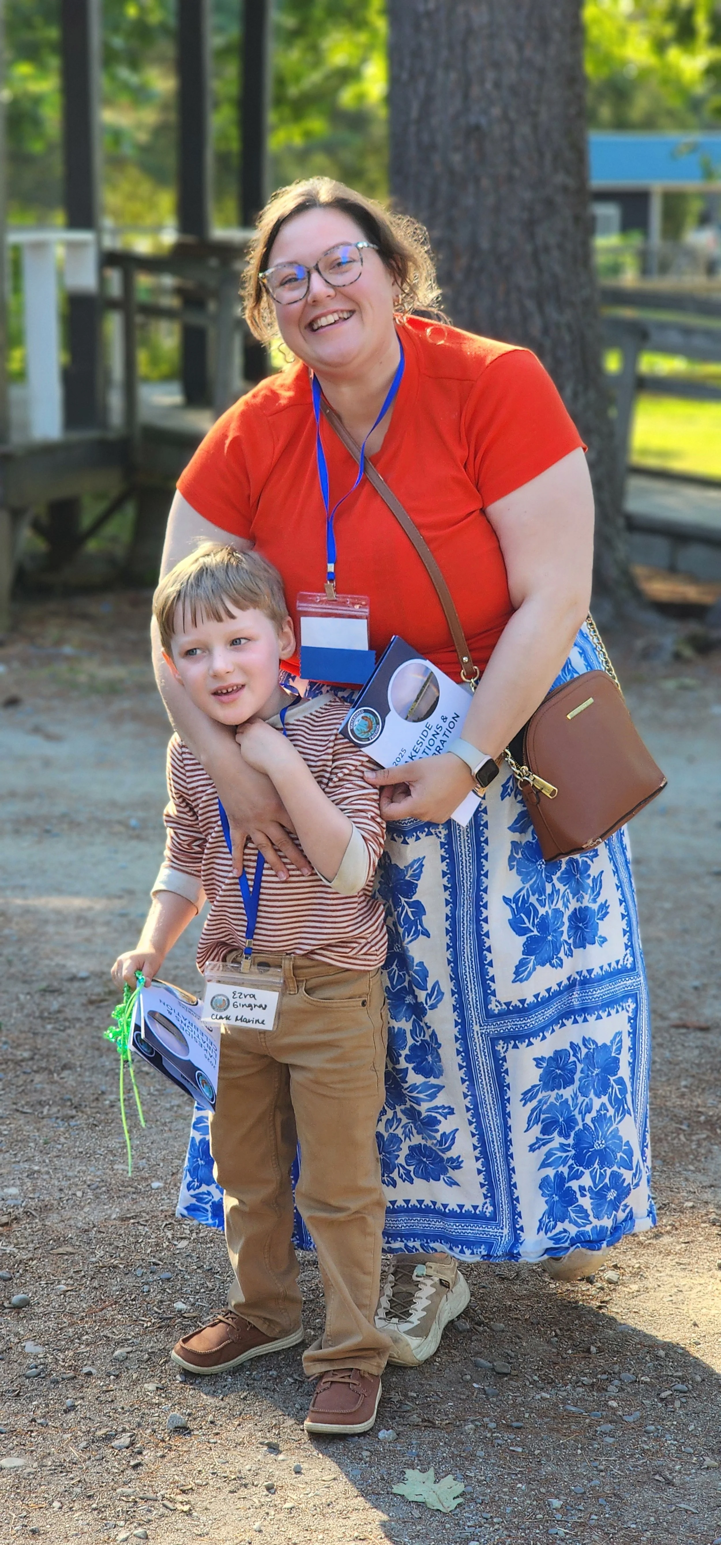 A woman, wearing a coral t-shirt and blue and white patterned skirt, and child wearing a brown and white striped shirt and brown pants