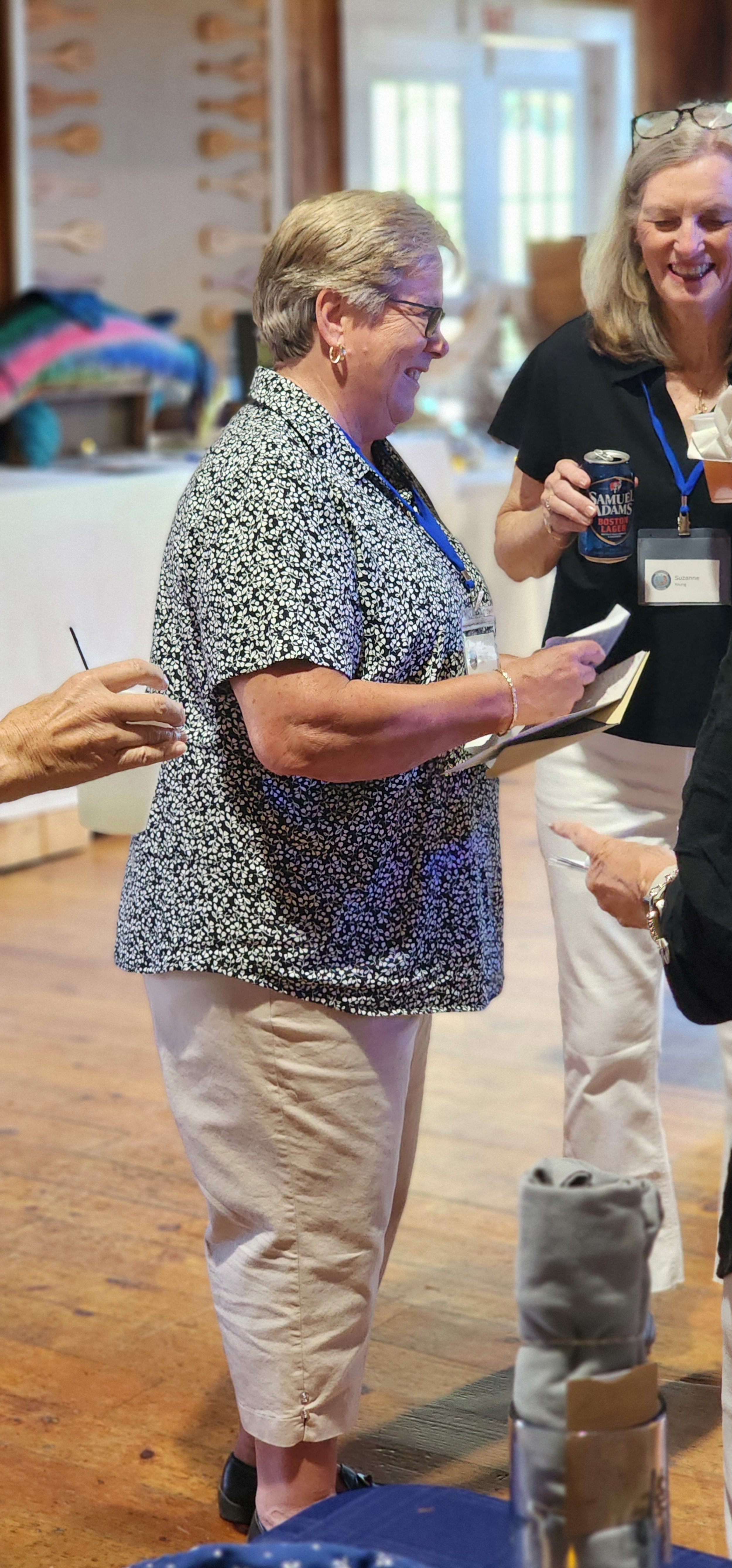 A woman, wearing a blue and white floral shirt and white pants, smiling off camera