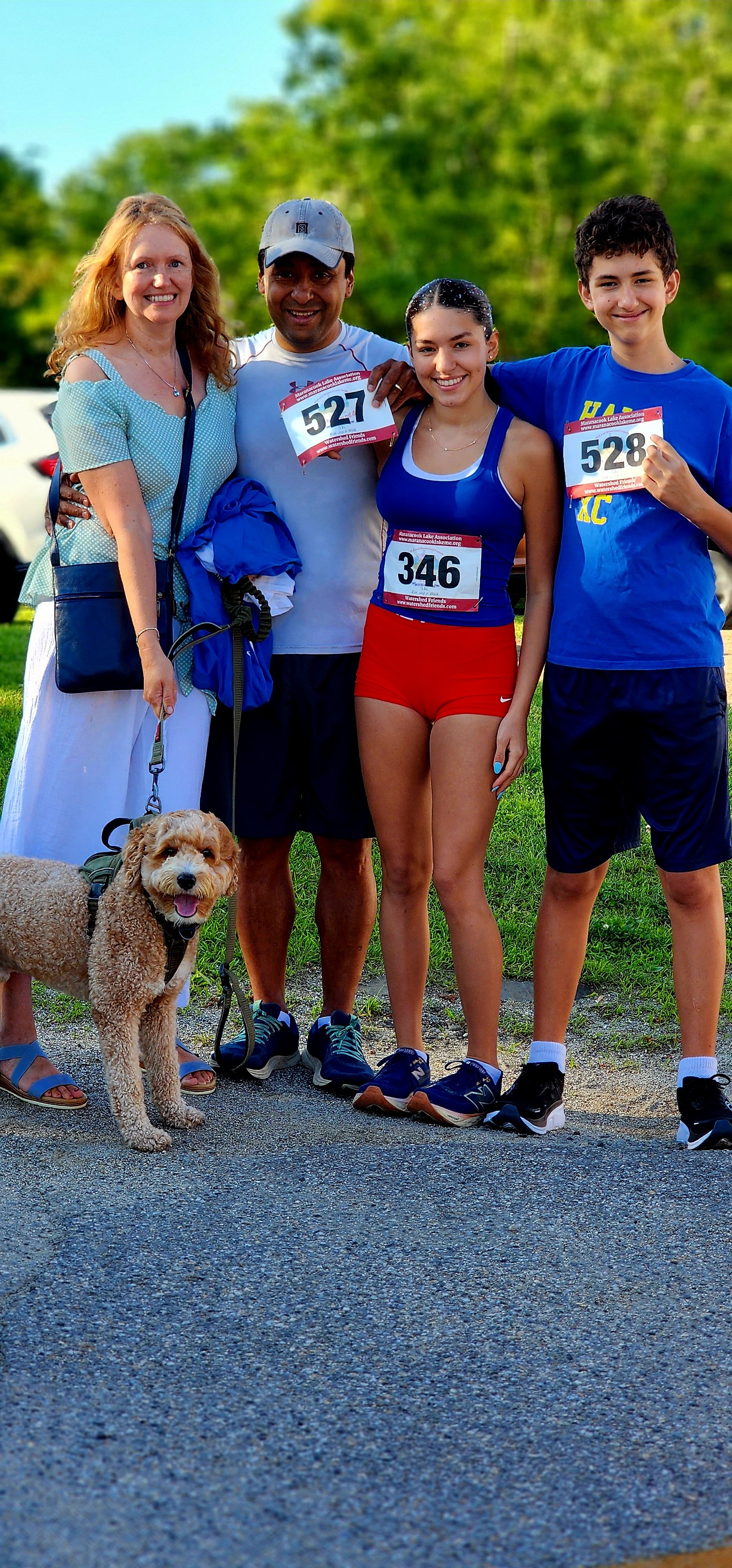 Four people and a dog smiling at the camera, three of the people have bib numbers