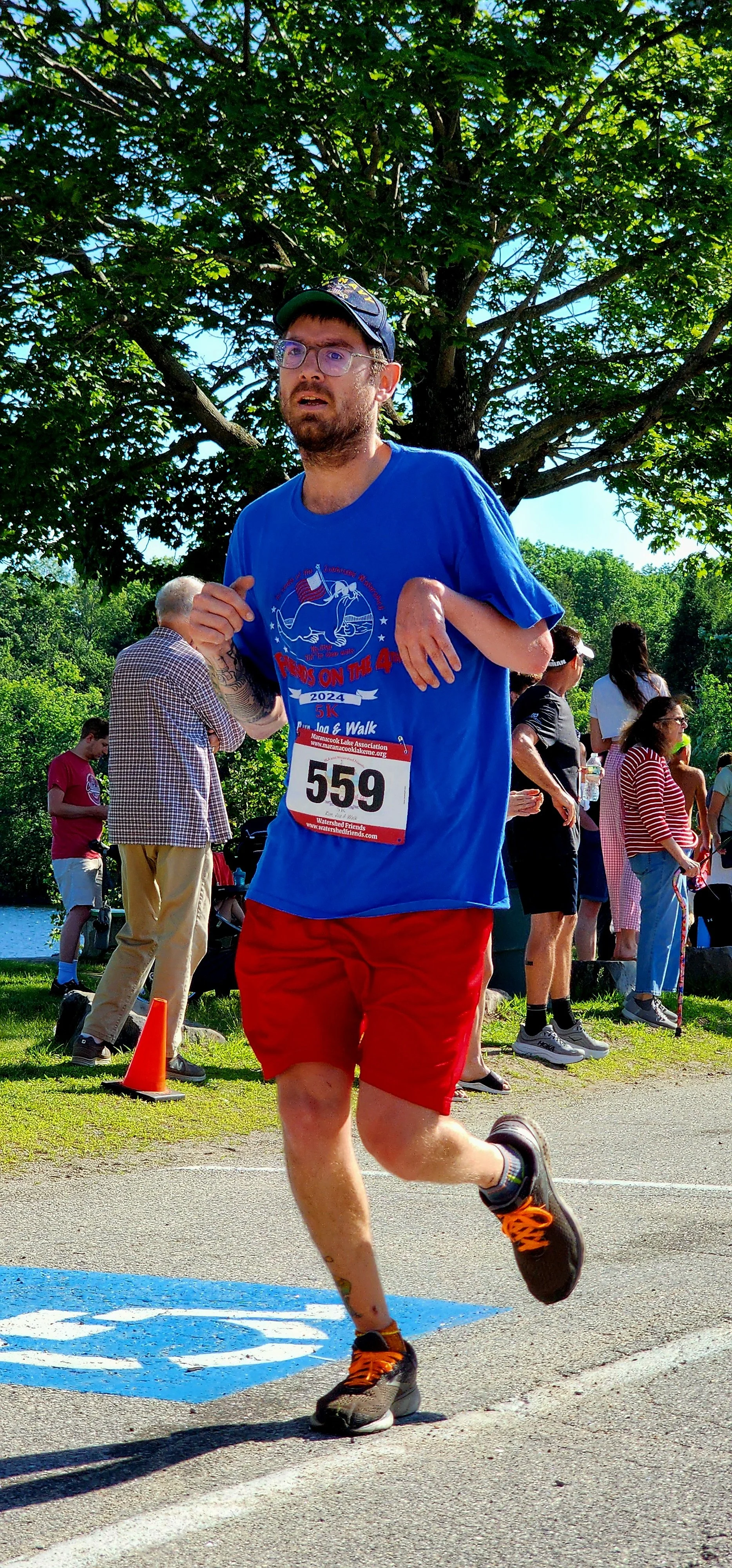 A man wearing a blue t-shirt with red shorts running with a crowd standing in the background