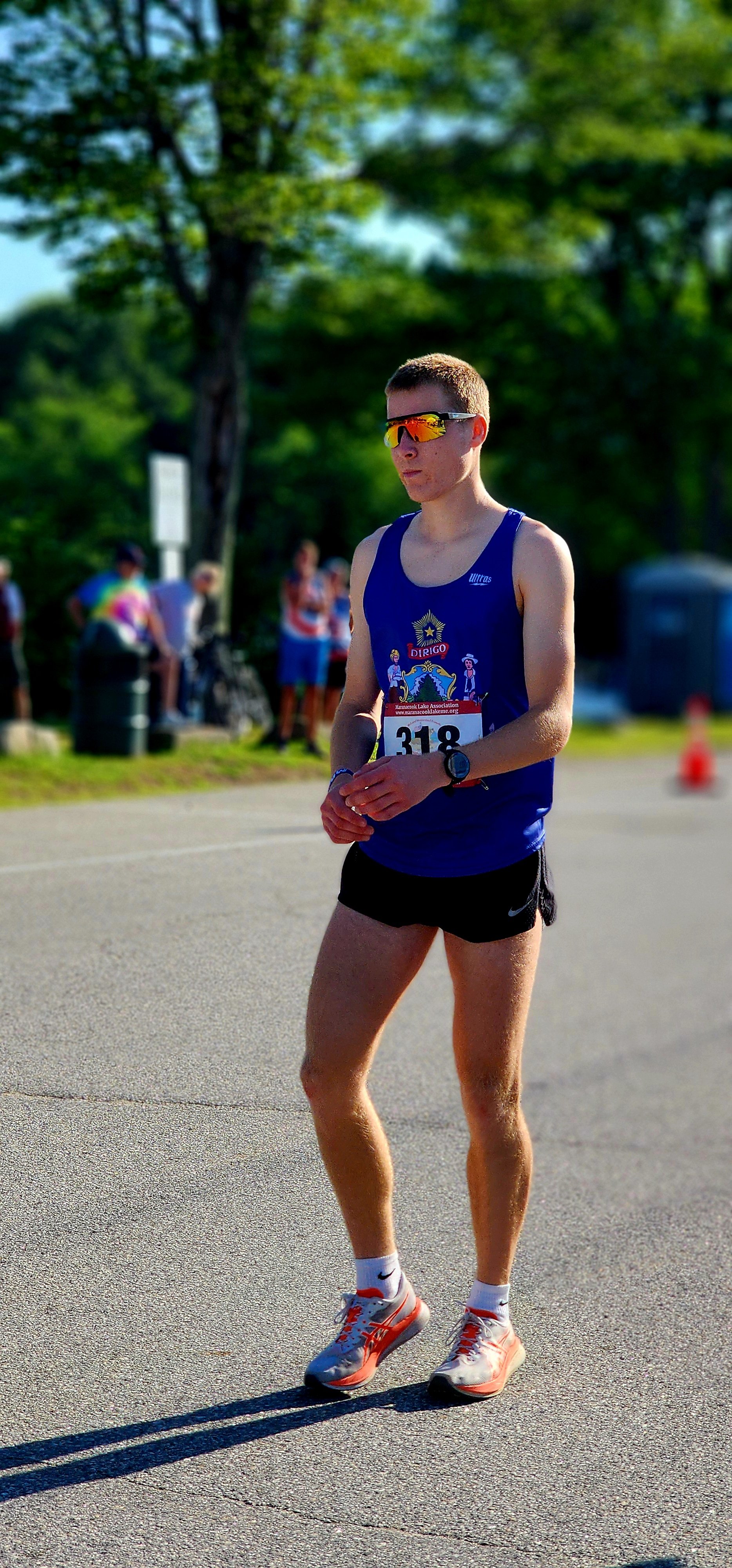 A man, wearing a blue tank top and black shorts, walking across pavement